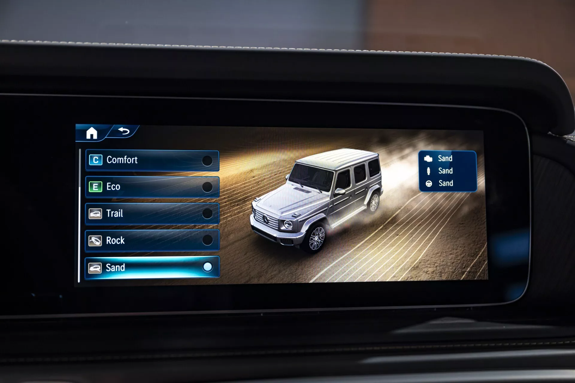 Wyświetlacz systemu infotainment Mercedes-Benz G-Klasse 2024 pokazujący tryb jazdy po piasku z cyfrowym przedstawieniem samochodu
