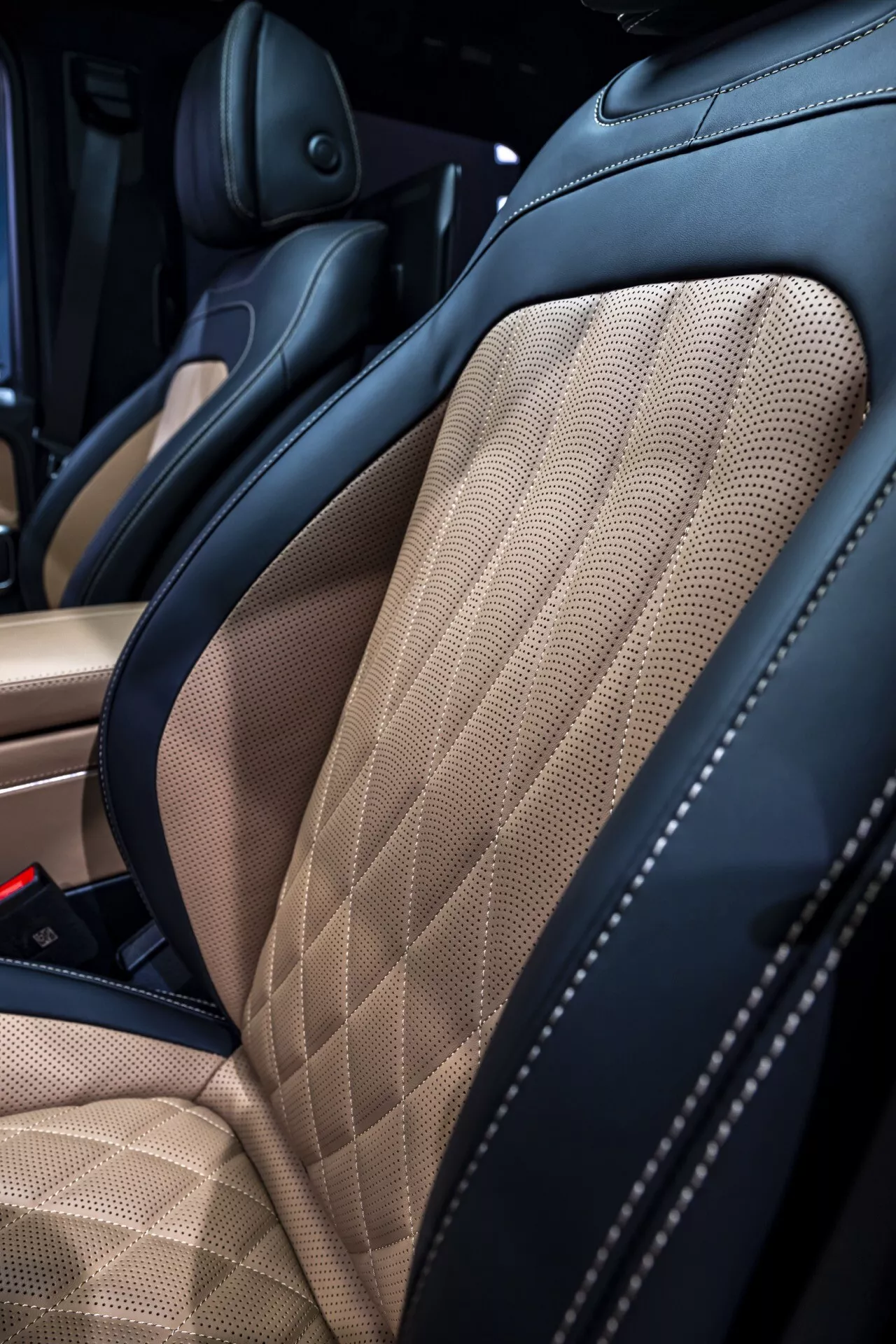 Zbliżenie wnętrza Mercedes-Benz G-Klasse 2024 skupiające się na wysokiej jakości dwukolorowym skórzanym siedzeniu z pikowaniem w romby i zwiększonym wsparciem bocznym