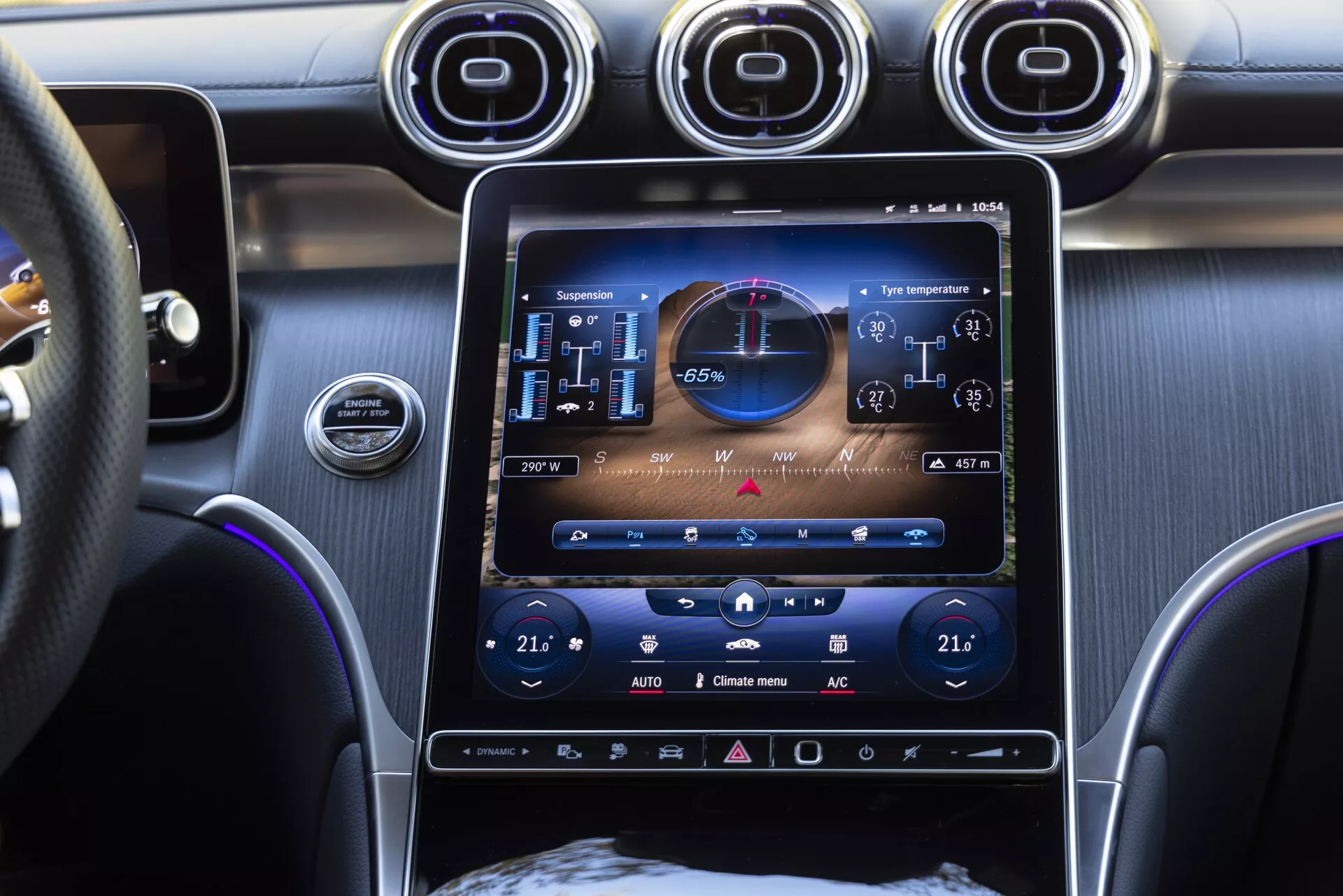 Zbliżenie na konsolę centralną Mercedes GLC 2022 z pionowym 10-12 calowym ekranem dotykowym systemu infotainment wyświetlającym stan pojazdu z cyfrowym prędkościomierzem, obrotomierzem i kontrolami klimatyzacji pokazującymi 21 stopni Celsjusza dla pasażera i kierowcy. Luksusowe wnętrze zawiera chromowane wloty powietrza, przycisk start/stop silnika, wielofunkcyjną skórzaną kierownicę i niebieskie oświetlenie ambientowe.