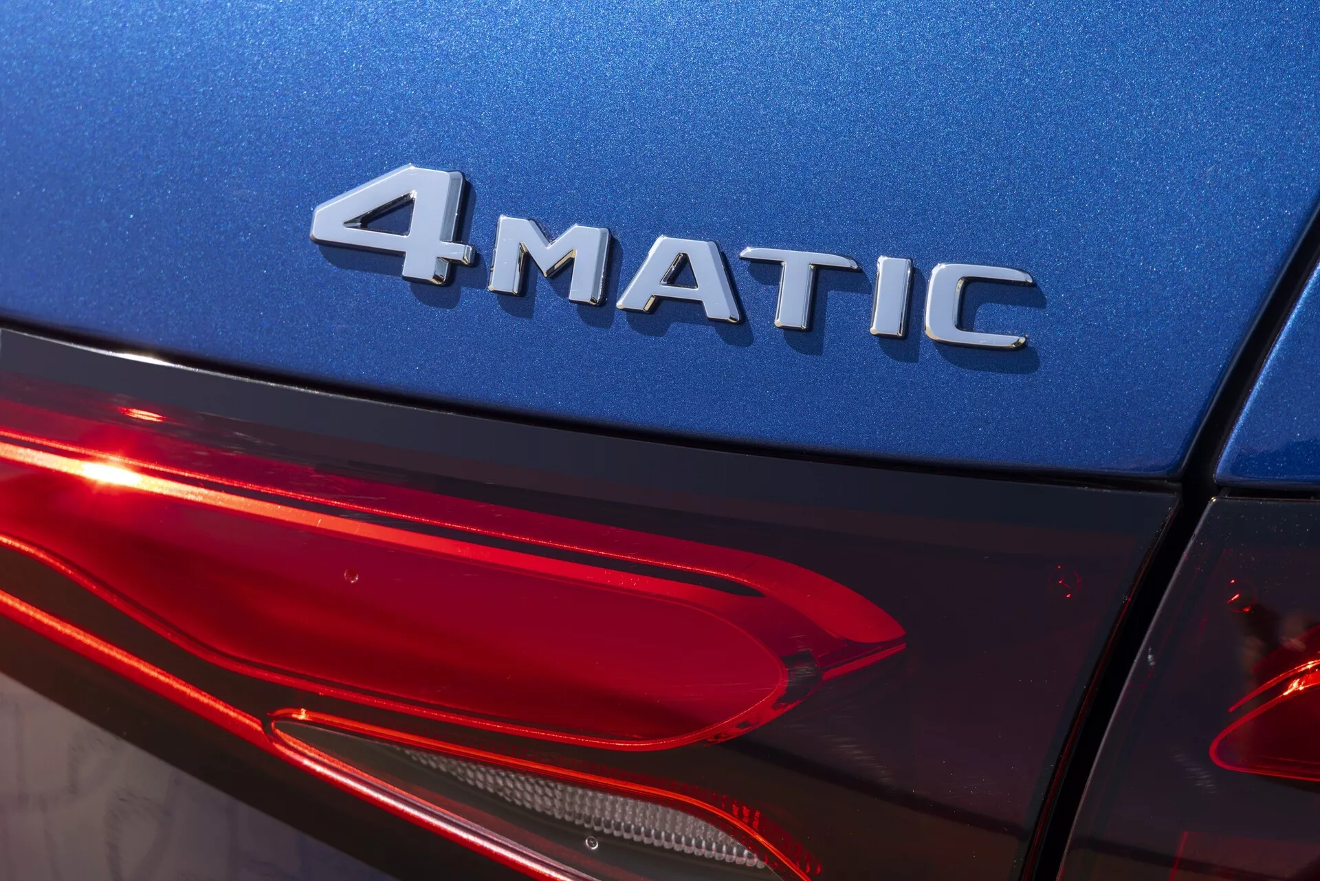 Zbliżenie na tylny kwartał Mercedesa GLC 2022 (254) pod lekkim kątem w górę, pokazujące emblemat 4MATIC, błyszczący niebieski lakier nadwozia i nowoczesny design tylnych świateł LED. Podkreśla technologię napędu na cztery koła, oświetlenie samochodowe i wysokiej jakości wykończenie zewnętrzne.