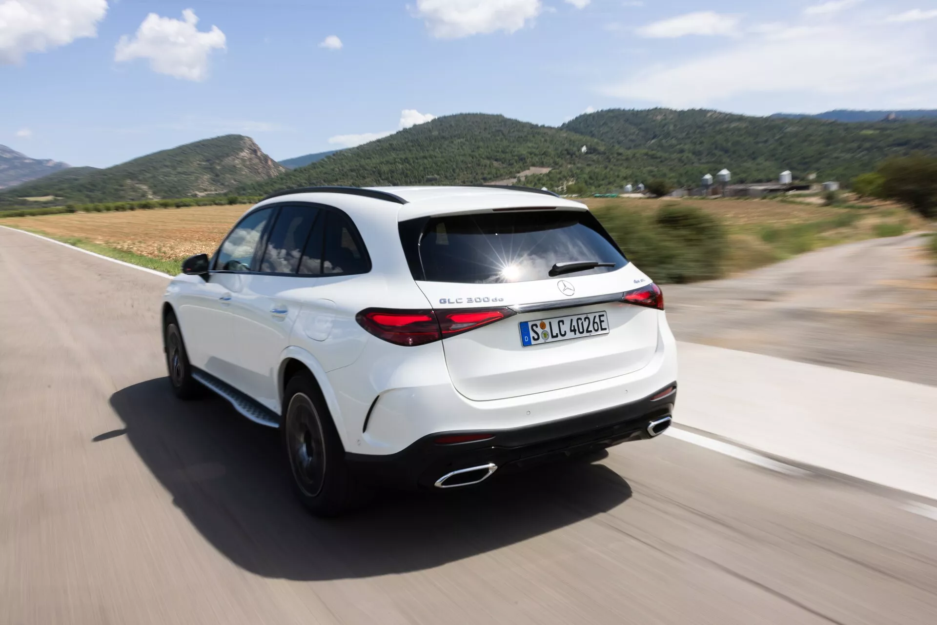 Dynamiczny widok tylno-boczny SUV-a Mercedes GLC 254 z 2022 roku w ruchu, z efektem panoramowania. Kąt kamery uchwyca elegancki design i nowoczesne tylne światła, ukazując prawy tylny kwartał, tylne światła, tylne koło oraz część prawego profilu bocznego na dobrze utwardzonej drodze. Podkreśla elektryczną/hybrydową wersję z oznaczeniem 'EQ', sportową sylwetkę, aerodynamiczne progi boczne, podwójne wydechy oraz linię dachu w stylu coupé. Rozmyte tło i koła podkreślają prędkość i ruch samochodu.