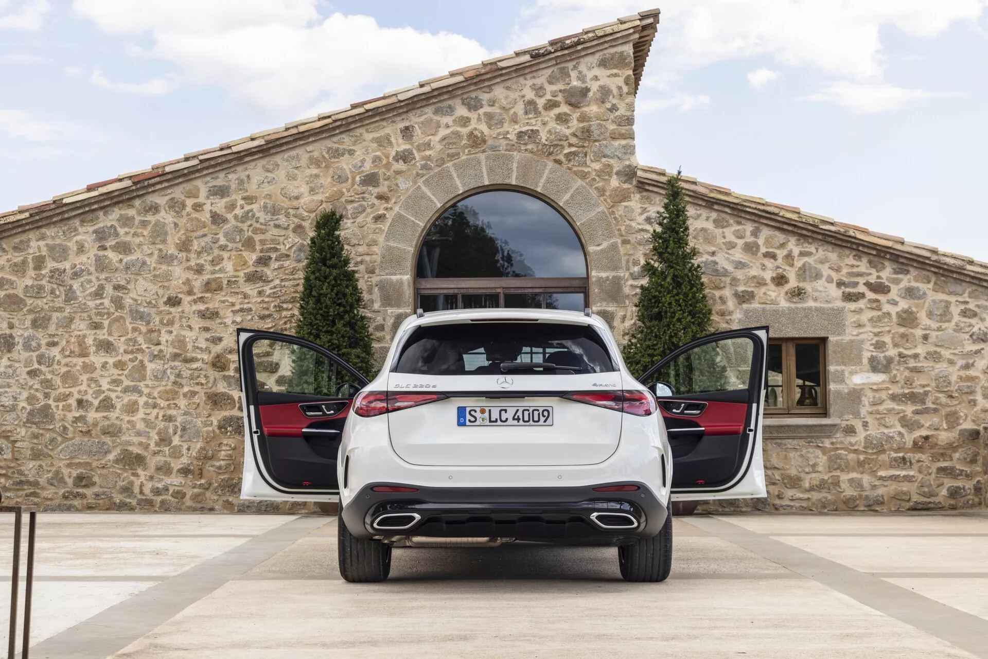 Widok tylny nieruchomego Mercedesa GLC 2022 z otwartym bagażnikiem i uchylonymi tylnymi drzwiami pasażerskimi, prezentującego system podwójnego wydechu, eleganckie tylne lampy LED, zamontowaną tablicę rejestracyjną, oznaczenie modelu oraz praktyczną płaską podłogę ładunkową z wewnętrznymi panelami drzwi tylnych z kontrastującym schematem kolorów i metalowymi wykończeniami.