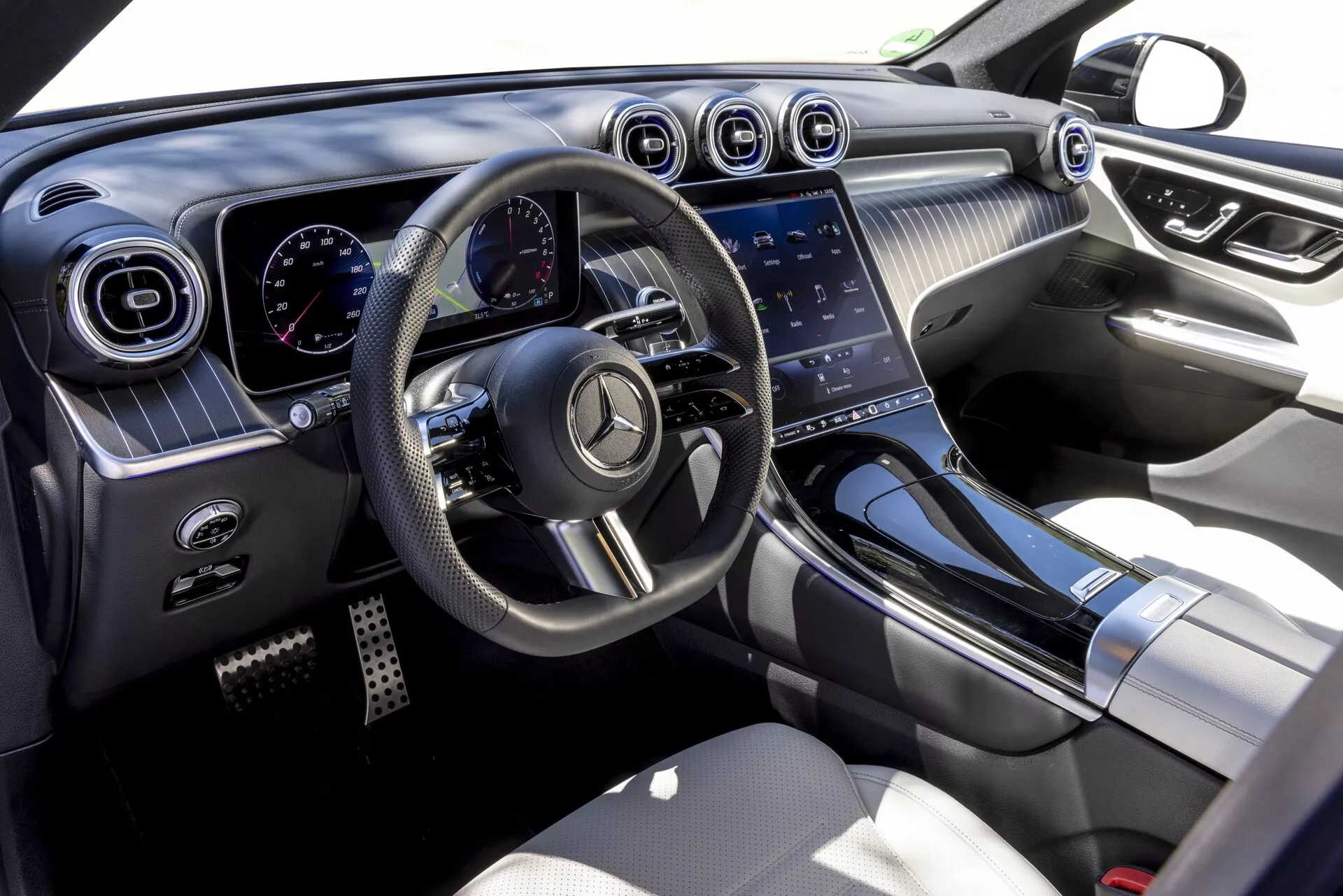 Widok wnętrza Mercedesa GLC 2022 (254) z perspektywy pasażera, ukazujący nowoczesny i luksusowy design z wielofunkcyjną kierownicą o spłaszczonym dole, cyfrowym panelem instrumentów, okrągłymi nawiewami z chromowanymi akcentami, dużym ekranem dotykowym systemu infotainment oraz wysokiej jakości materiałami, takimi jak miękkie w dotyku powierzchnie, metaliczne akcenty i skórzane fotele.