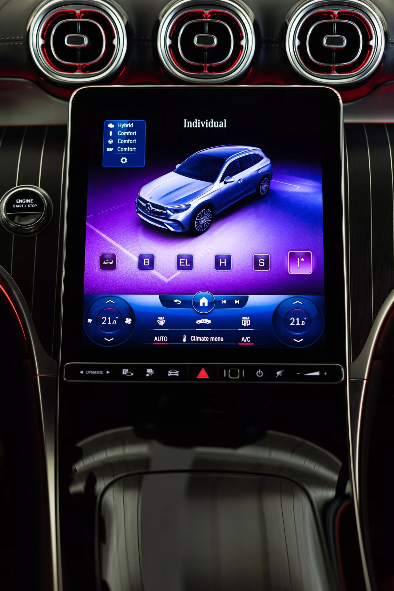 Cyfrowa ilustracja na ekranie systemu informacyjno-rozrywkowego Mercedesa GLC 2022, przedstawiająca niebieskiego sedana z wysokiej perspektywy 3/4 przodu, otoczona fizycznymi elementami sterującymi klimatyzacją oraz trzema okrągłymi wlotami powietrza z czerwonymi podświetlanymi obręczami w nowoczesnym i sportowym czarnym wnętrzu z metalicznymi akcentami, widziana z fotela kierowcy.