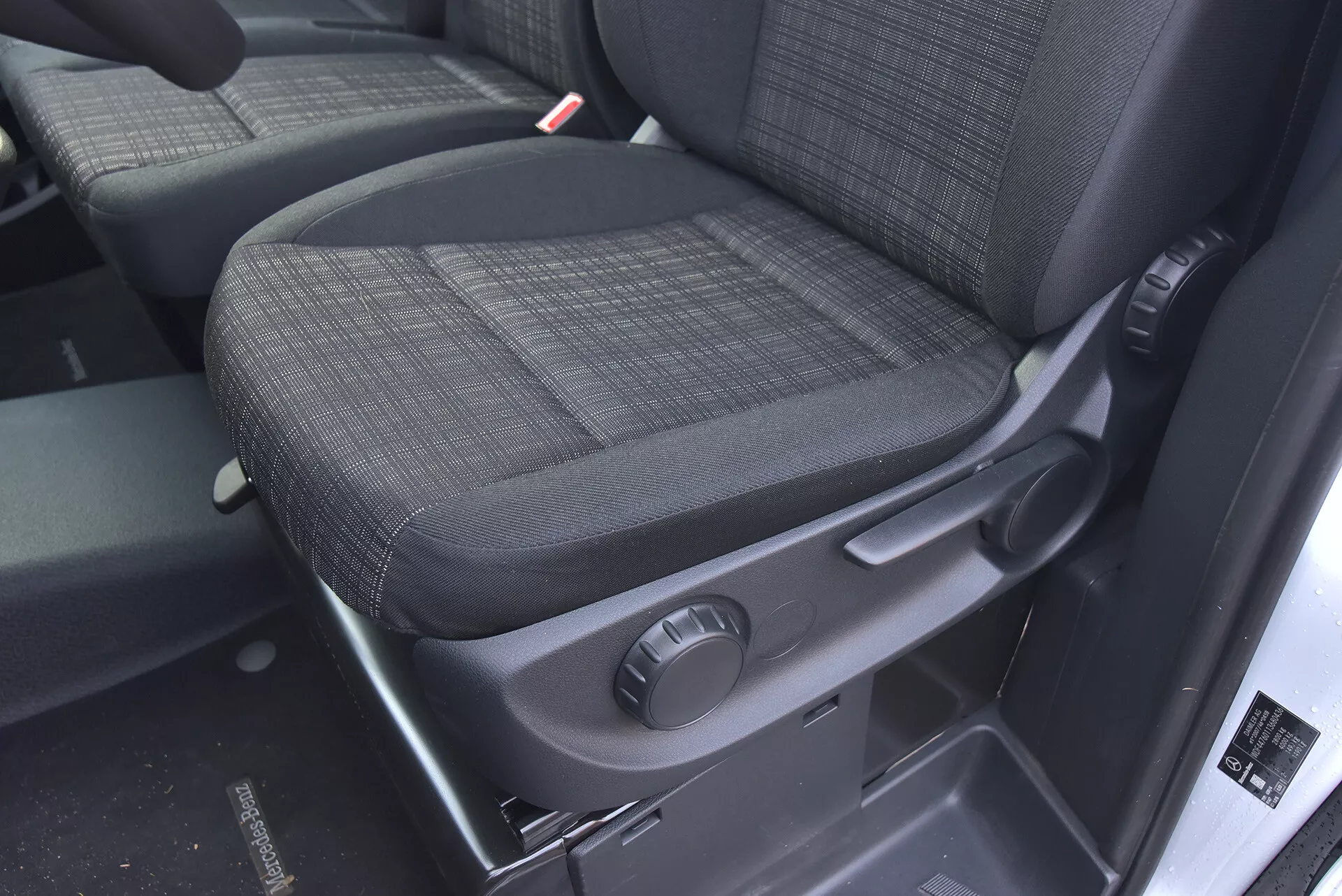 Wnętrze Mercedes-Benz Vito 2014 Tourer skupiające się na siedzeniu pasażera z trwałą, ciemną tapicerką, pokrętłem do manualnej regulacji oraz funkcjami bezpieczeństwa, takimi jak wyraźnie widoczny odbiornik pasa bezpieczeństwa.