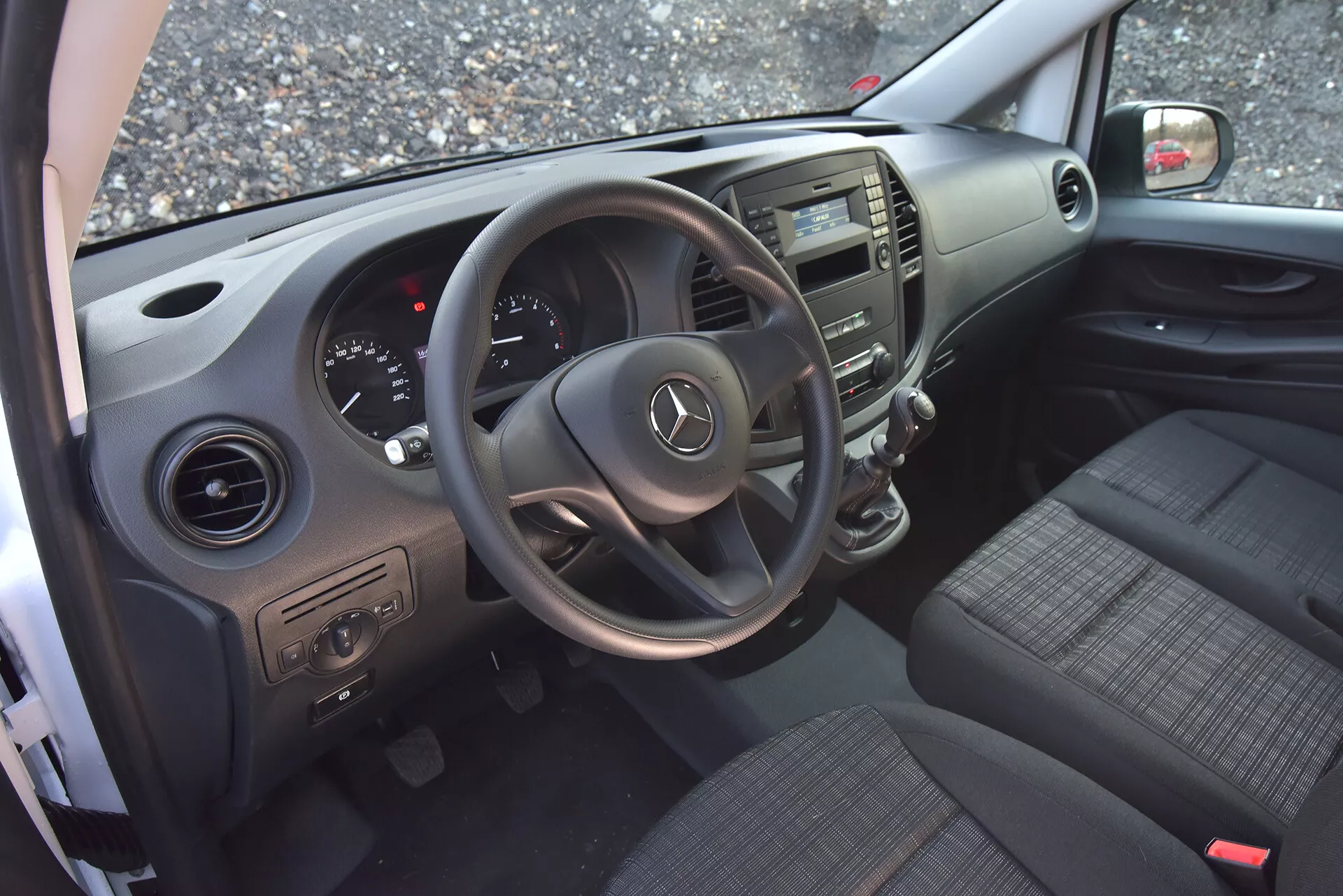 Wnętrze Mercedes-Benz Vito Tourer z 2014 roku widziane z otwartych drzwi kierowcy, podkreślające kierownicę z logo Mercedes, zespół wskaźników, konsolę środkową, siedzenia z tkaniny, panele drzwiowe i nawiewy.