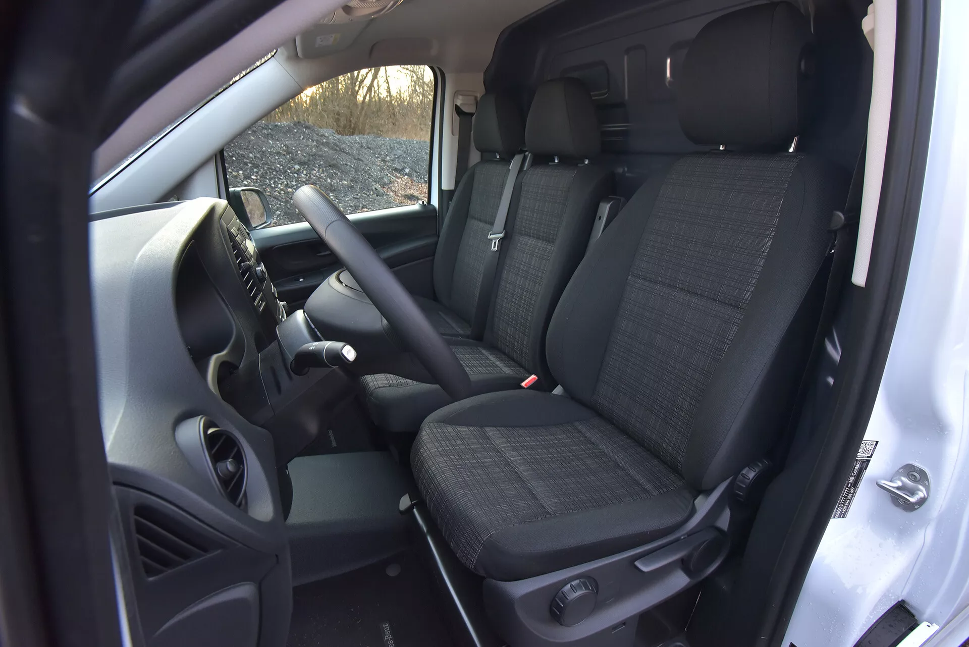 Wnętrze Mercedes-Benz Vito 2014 (Vito-Tourer) pokazujące obszar kierowcy i pasażera z przodu z cechami technologicznymi takimi jak sterowanie zamontowane na kierownicy, centralna konsola potencjalnie zawierająca system infotainment, przednie siedzenia z tkaniny wzorzystej z zagłówkami, i widok na tylne siedzenia, wszystko ujęte z wysokiego punktu widzenia podkreślającego przestronność kabiny i elementy manualnej skrzyni biegów.