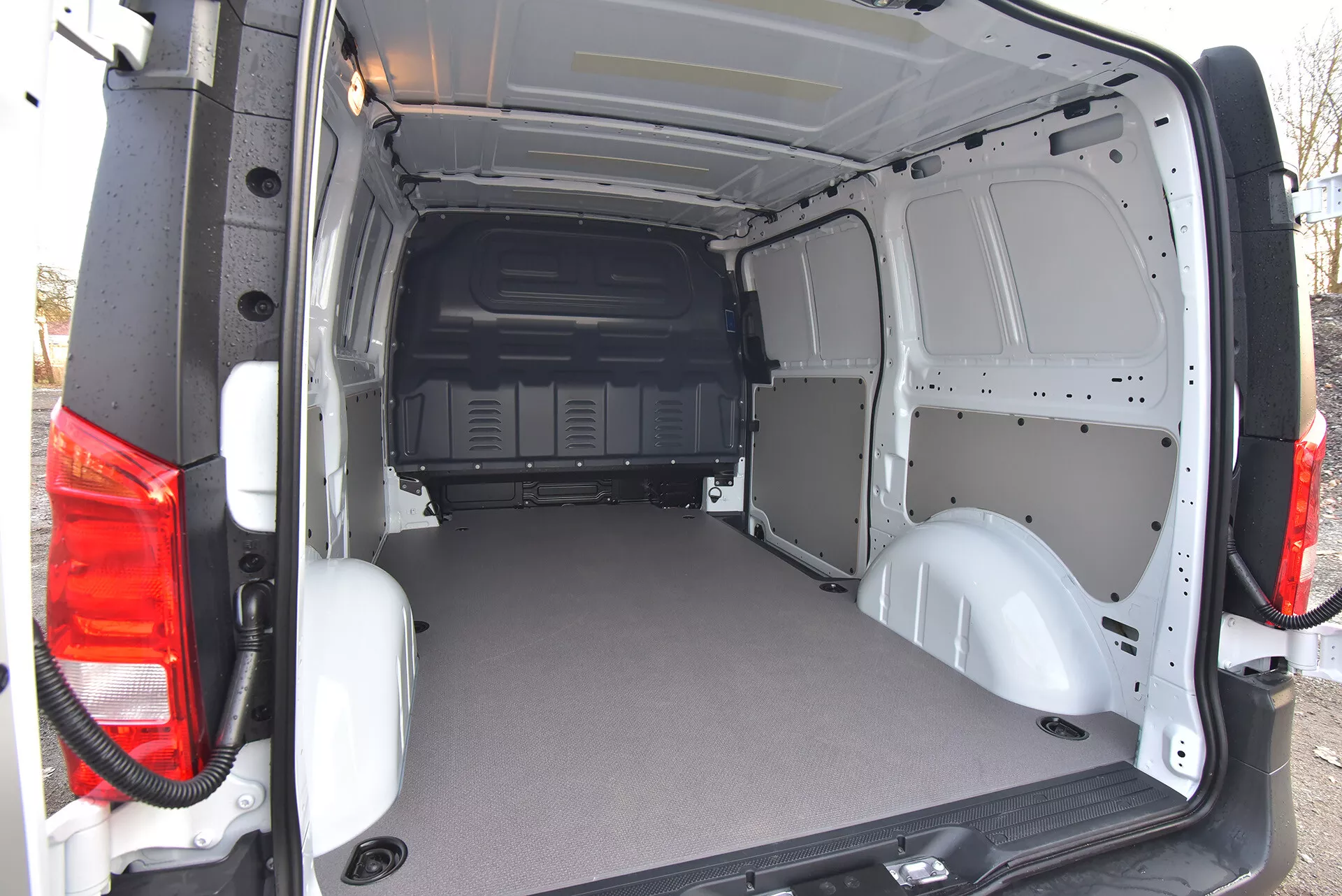 Tylna przestrzeń ładunkowa dostawczego vana Mercedes-Benz Vito Tourer z 2014 roku z otwartymi drzwiami, prezentująca płaską, wytrzymałą podłogę i goły metalowy wnętrze dla łatwej modyfikacji, widok z zewnętrznego skośnego kąta od tyłu
