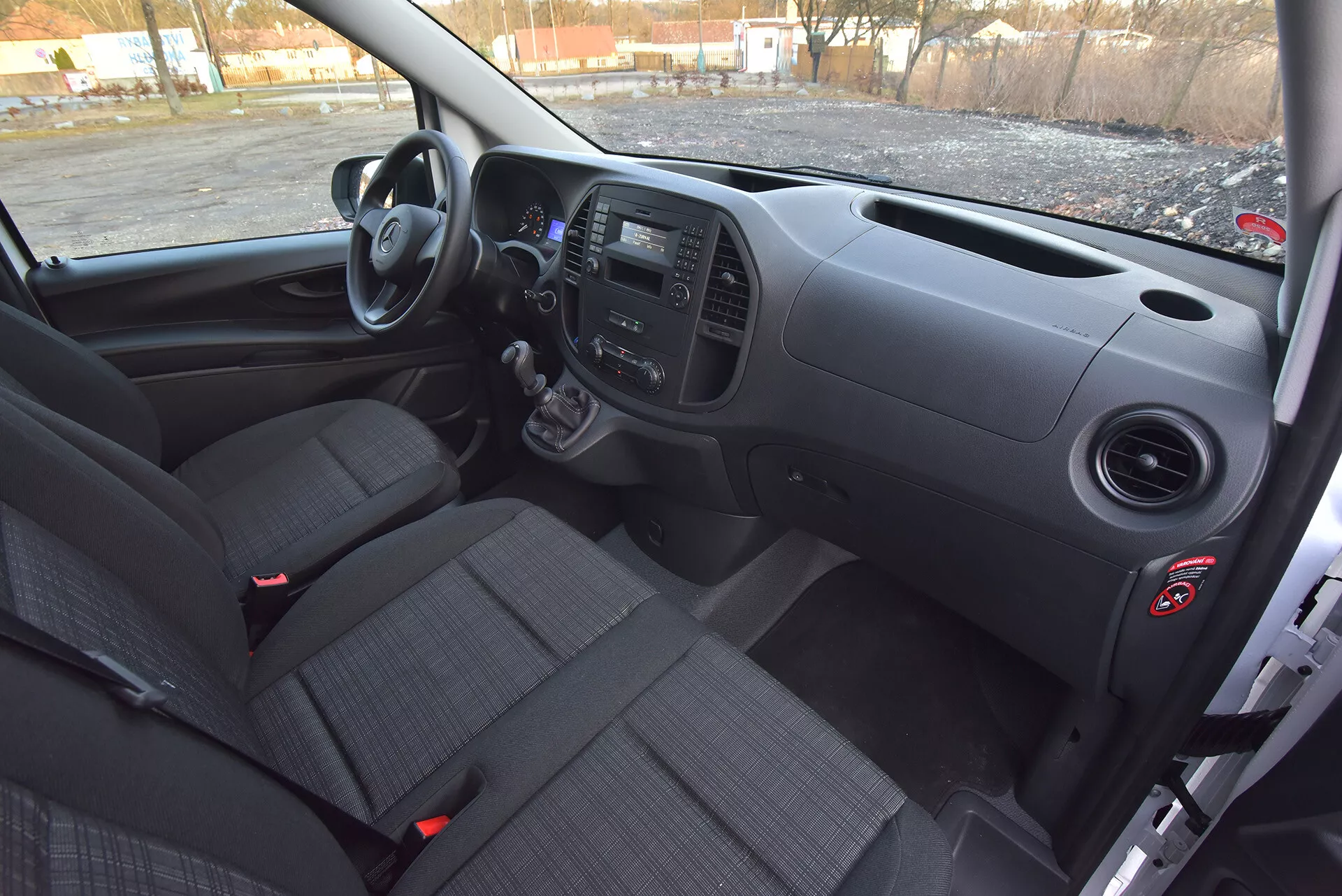 Widok wnętrza Mercedes-Benz Vito Tourer z 2014 roku od strony kierowcy, pokazujący przednią deskę rozdzielczą, manualną skrzynię biegów, panele kontrolne i siedzenia tapicerowane