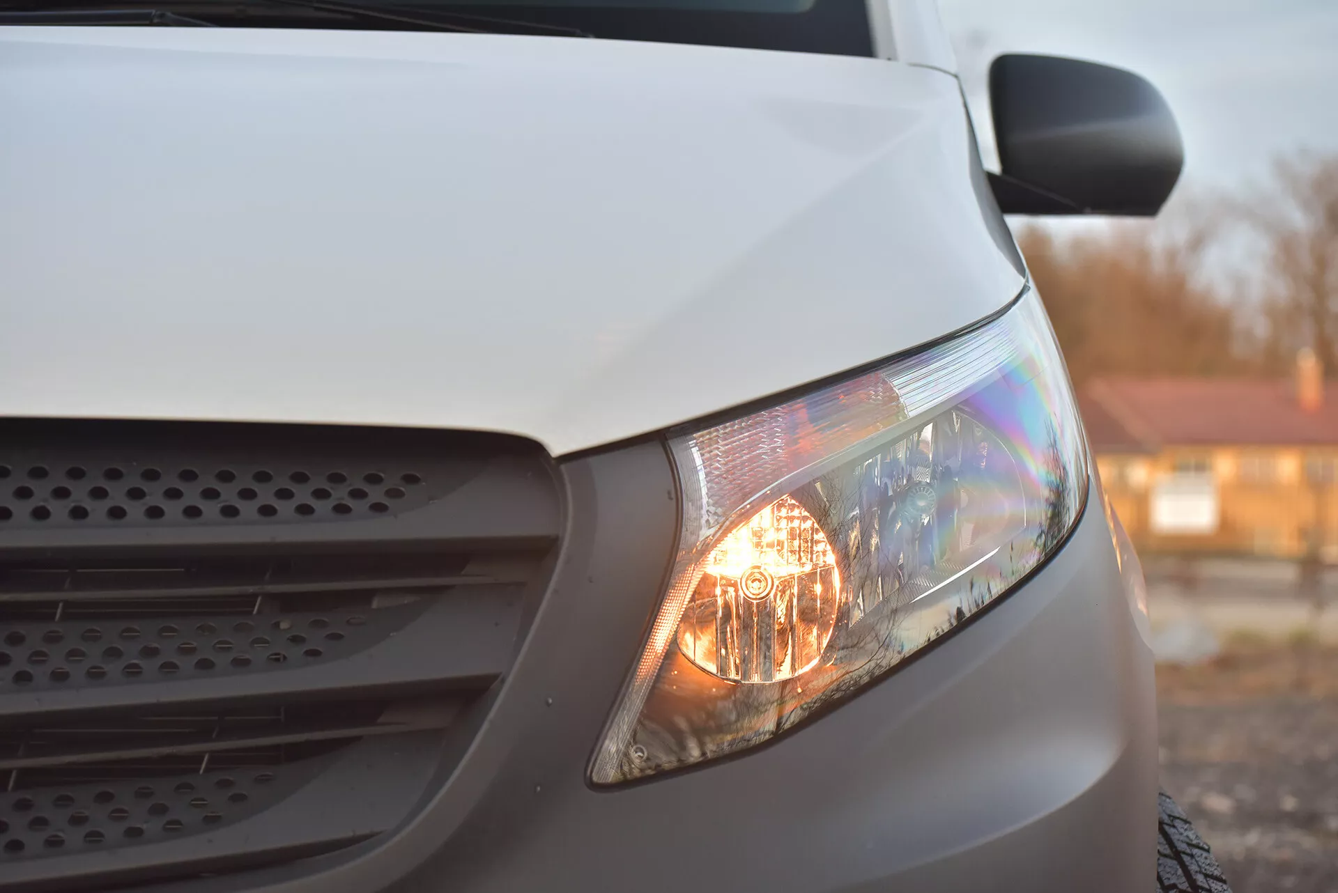 Zbliżenie boczne białego Mercedesa-Benz Vito Tourer z 2014 roku skupione na świecącym reflektorze, części grilla i sekcji maski, podkreślające jego halogenowe reflektory i aerodynamiczny projekt w miękkim świetle.