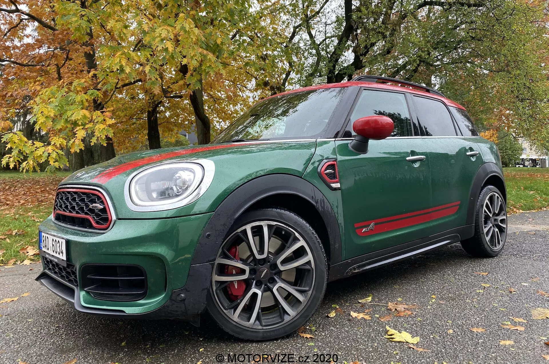 Niskokątowy przedni widok z trzech czwartych na Mini Countryman John Cooper Works 2020, ukazujący ciemnozielony wygląd zewnętrzny z czerwonymi akcentami, sportowymi wieloramiennymi kołami, kratką otoczoną chromem, dużymi wlotami powietrza, reflektorami LED i czerwonymi zaciskami hamulcowymi.