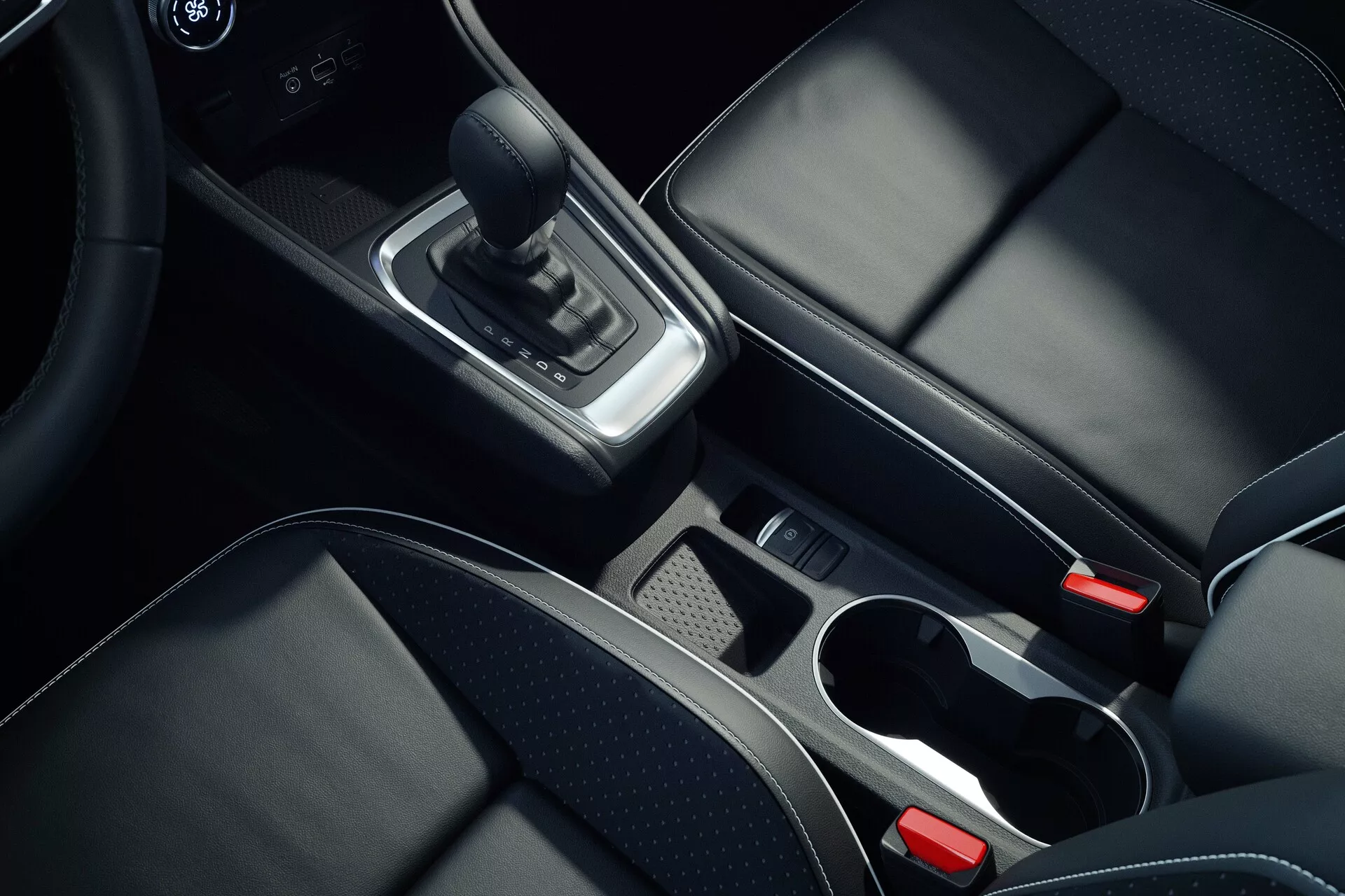 Wnętrze konsoli środkowej drugiej generacji Mitsubishi ASX 2023, widziane z lotu ptaka, skupiające się na szczegółach takie jak skórzana dźwignia zmiany biegów, chromowane akcenty wokół obszaru zmiany biegów, schowek z wyjmowaną tacką, dwa uchwyty na kubki z chromowanymi obrączkami, czarne skórzane fotele z widocznymi szwami, przycisk elektronicznego hamulca postojowego i częściowo widoczny podłokietnik centralny pokazujący wysoką jakość materiałów i nowoczesne wzornictwo.