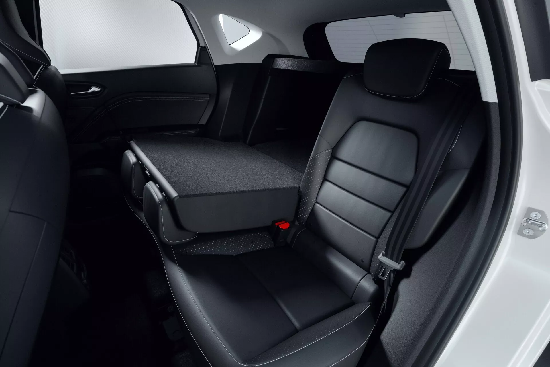 Widok wnętrza tylnej części siedzeń Mitsubishi ASX 2023 (2. generacja) z czarnymi, skórzanymi fotelami tylnymi wyposażonymi w zagłówki i szczegółowe przeszycia. Częściowo złożone środkowe siedzenie odsłania uchwyty na napoje lub schowek, podkreślając projekt dzielonego składanego siedzenia 60/40. Otwarte krawędzie drzwi pasażera ukazują elementy designu panelu drzwiowego. Zdjęcie koncentruje się na komforcie, jakości materiałów i wygodzie funkcji, spełniając nowoczesne standardy bezpieczeństwa, w tym trzy-punktowe pasy bezpieczeństwa.