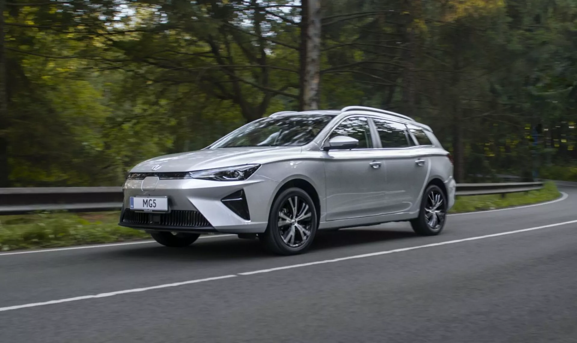 Mitsubishi Outlander Plug-In Hybrid 2018 w ruchu na drodze otoczonej drzewami, prezentujący swój elegancki design i reflektory LED, z rozmazanym zielonym tłem podkreślającym szybkość i ekologiczną technologię.