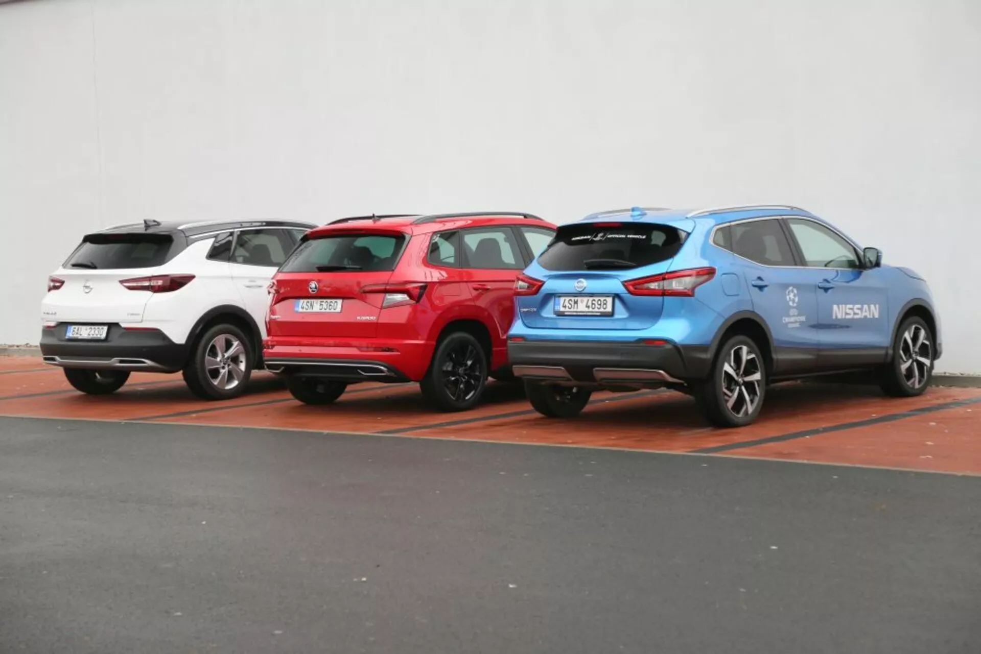Trzy SUVy Nissan Qashqai z 2014 roku w kolorach białym, czerwonym i niebieskim zaparkowane obok siebie, prezentujące tylne i boczne profile z widocznymi światłami tylnymi, wycieraczkami szyby tylnej i sportowymi felgami aluminiowymi na niewyróżniającym się tle.