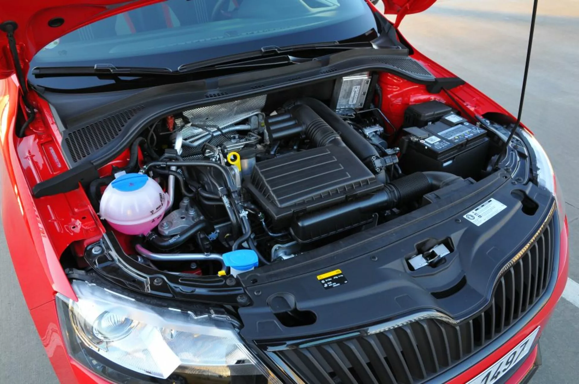 Zbliżony widok otwartej komory silnika Opla Astry 2005 (Astra TwinTop), podkreślający komponenty mechaniczne takie jak skrzynia dolotowa powietrza, pokrywa silnika, zbiorniki płynu chłodzącego i hamulcowego oraz bateria z lekko podniesionej perspektywy frontalnej