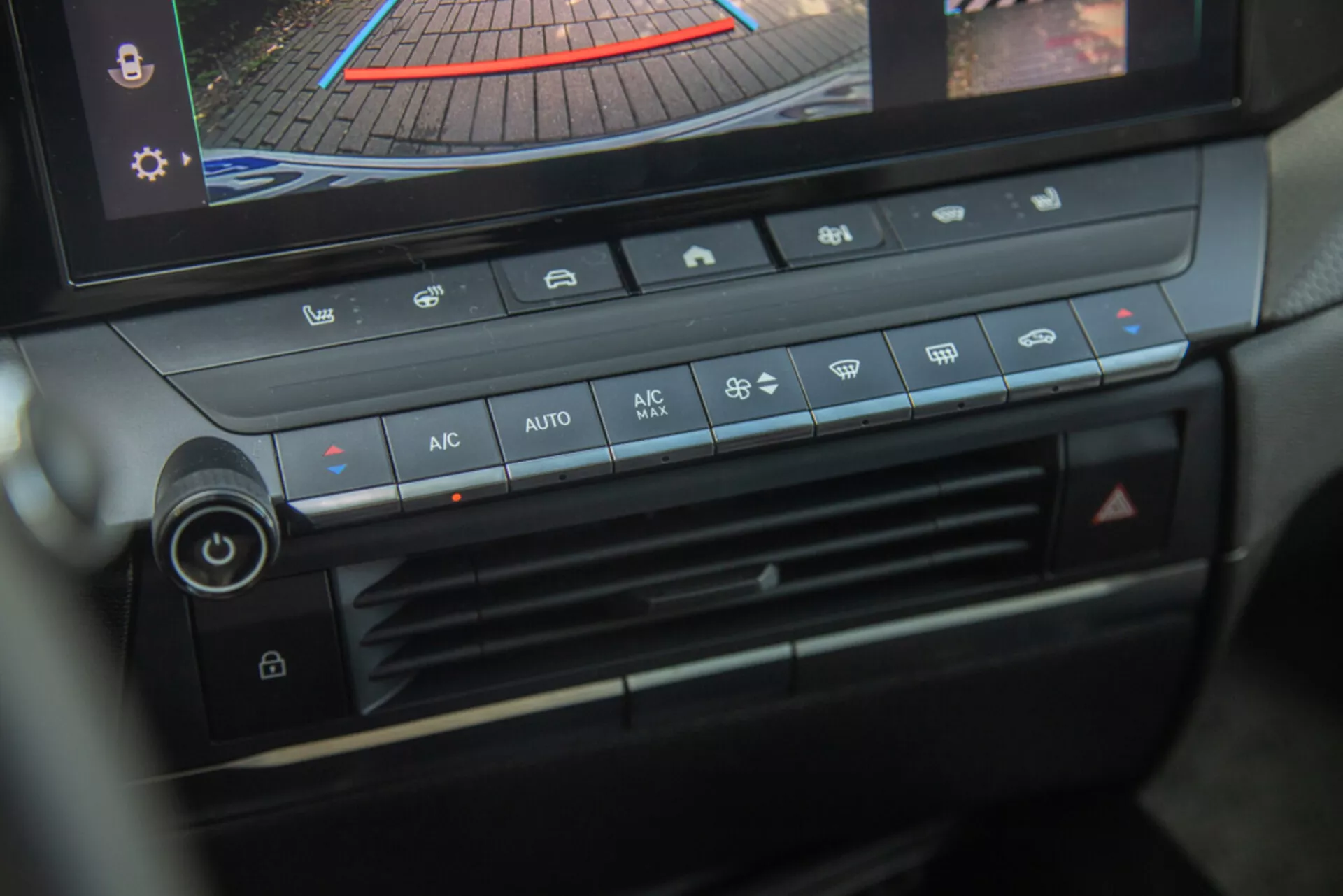 Centralna konsola i panel klimatyzacji Opel Astra 2022, podkreślające pokrętło regulacji temperatury, prędkość wentylatora, dystrybucję powietrza i przyciski automatycznej klimatyzacji z cyfrowym wyświetlaczem pokazującym kamerę cofania