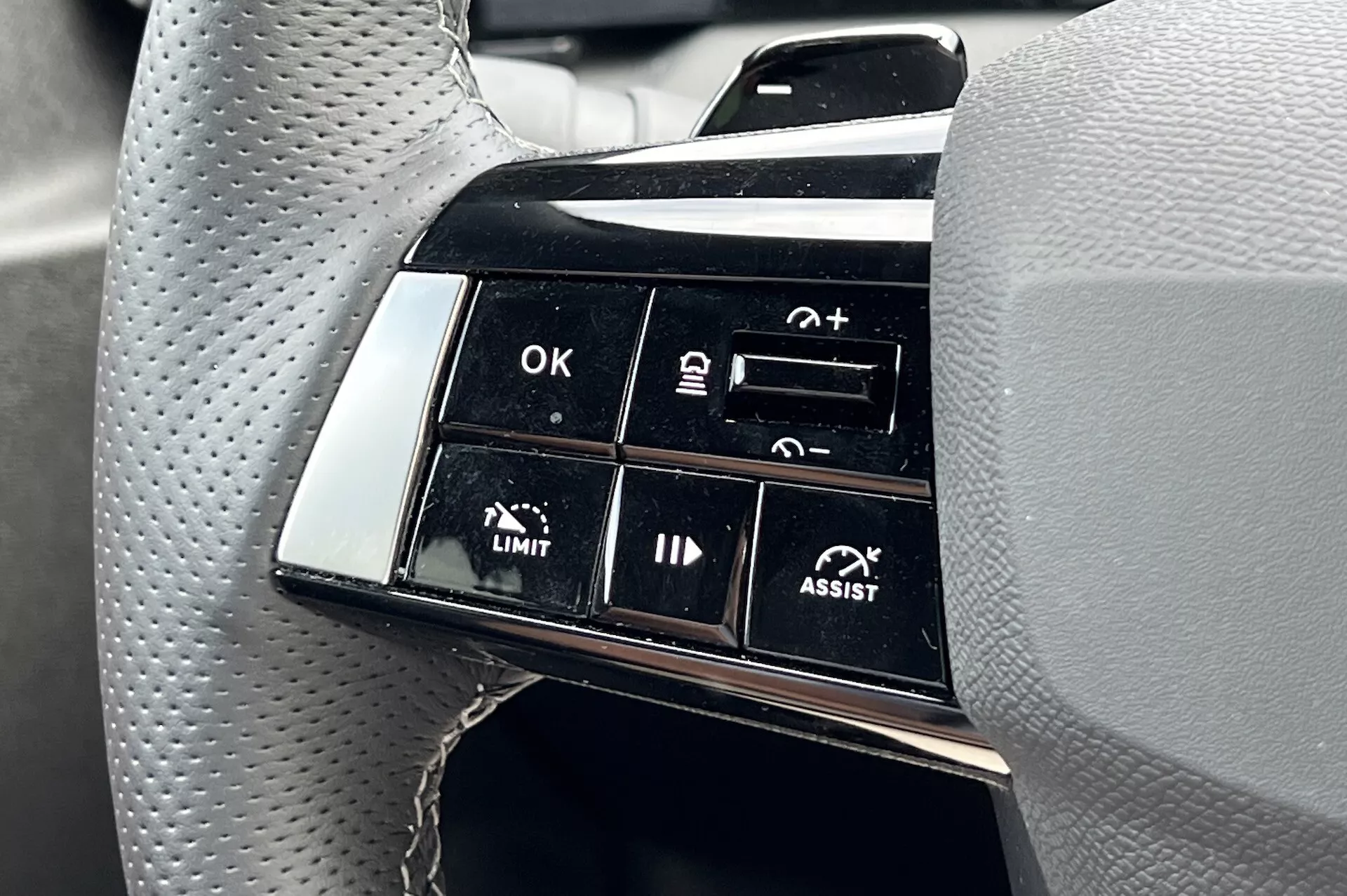 Zbliżenie na zespół przycisków na kierownicy Opel Astra 2022 podkreślające zaawansowane funkcje wspomagania jazdy, w tym adaptacyjny tempomat i asystent utrzymania pasa ruchu, ze skupieniem na etykietach funkcjonalnych takich jak OK, +, -, LIMIT i ASSIST z perspektywy kierowcy