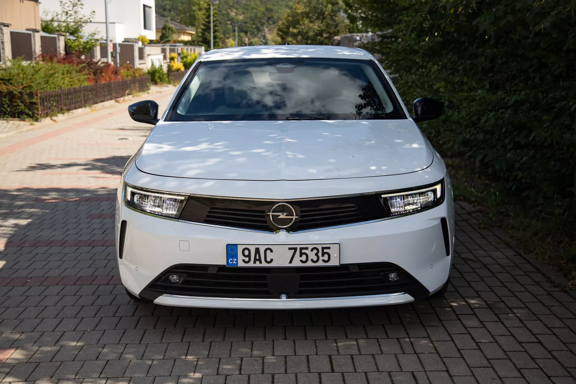 Przedni widok Opla Astry 2022 ukazujący nowoczesny design elektrycznego pojazdu z reflektorami LED, dekoracyjną kratką i aerodynamicznym kształtem, zaparkowany na podjeździe przydomowym