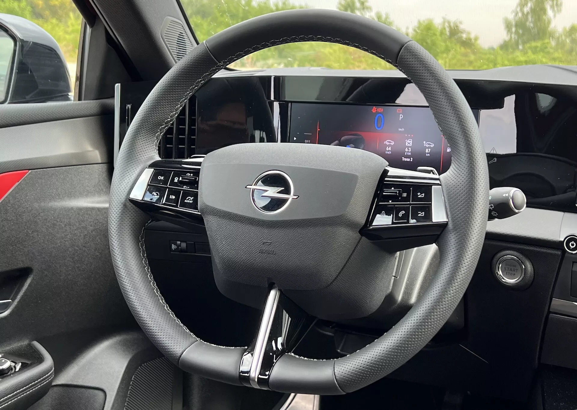 Szczegółowy widok wnętrza kierownicy Opel Astra 2022 z trójramiennym designem z wbudowanymi przyciskami kontrolnymi i w pełni cyfrowym wyświetlaczem deski rozdzielczej za nią, podkreślający nowoczesną technologię i ergonomię pojazdu