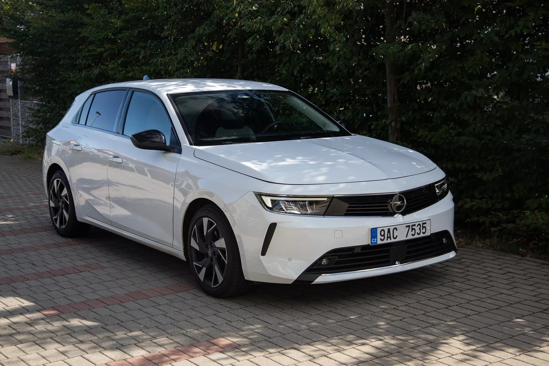 Biały Opel Astra 2022 z wyrazistym przodem, smukłymi reflektorami, poziomą kratą, aerodynamicznym zderzakiem, konturowaną maską i felgami ze stopu o wielu szprychach, uchwycony z perspektywy trzy czwarte z przodu na zewnątrz w ciągu dnia