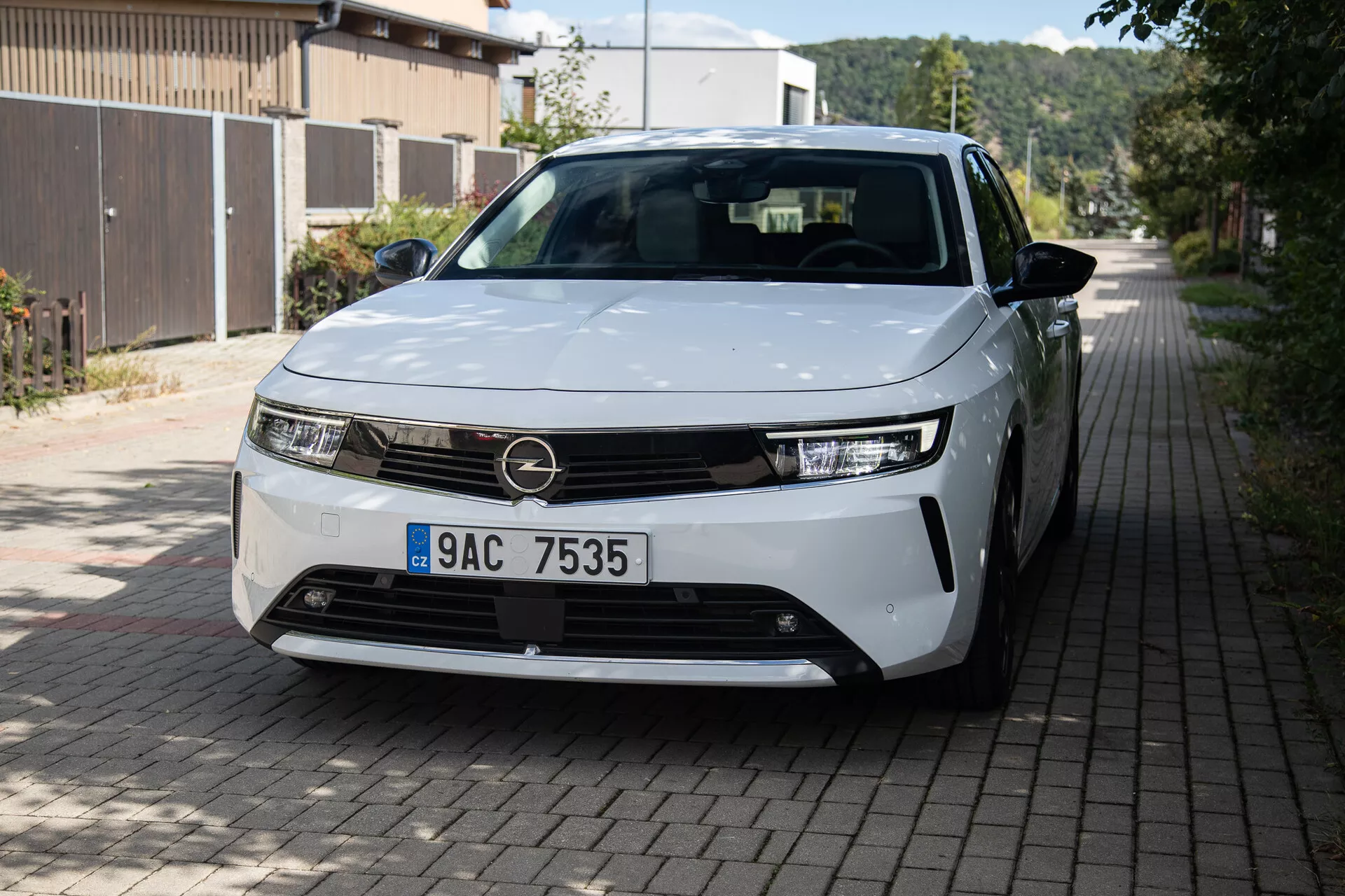 Widok z przodu i częściowo z boku na Opel Astra 2022 z LEDowymi światłami, minimalistycznym designem grilla, częściowo widocznymi kołami ze stopu i gładkimi panelami nadwozia na europejskiej ulicy mieszkalnej