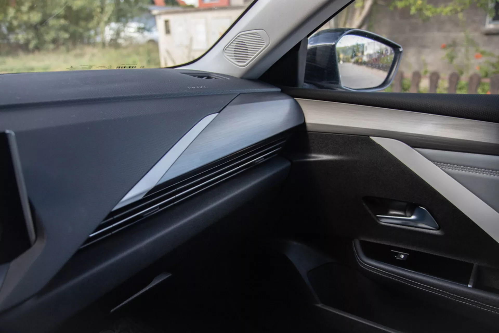 Widok wnętrza z perspektywy miejsca pasażera pokazujący projekt deski rozdzielczej, wykończenia oraz panel drzwi w Opel Astra 2022, przedstawiający ciemne, eleganckie linie konturowe ze skupieniem na teksturze materiałów i potencjalnych integracjach technologicznych