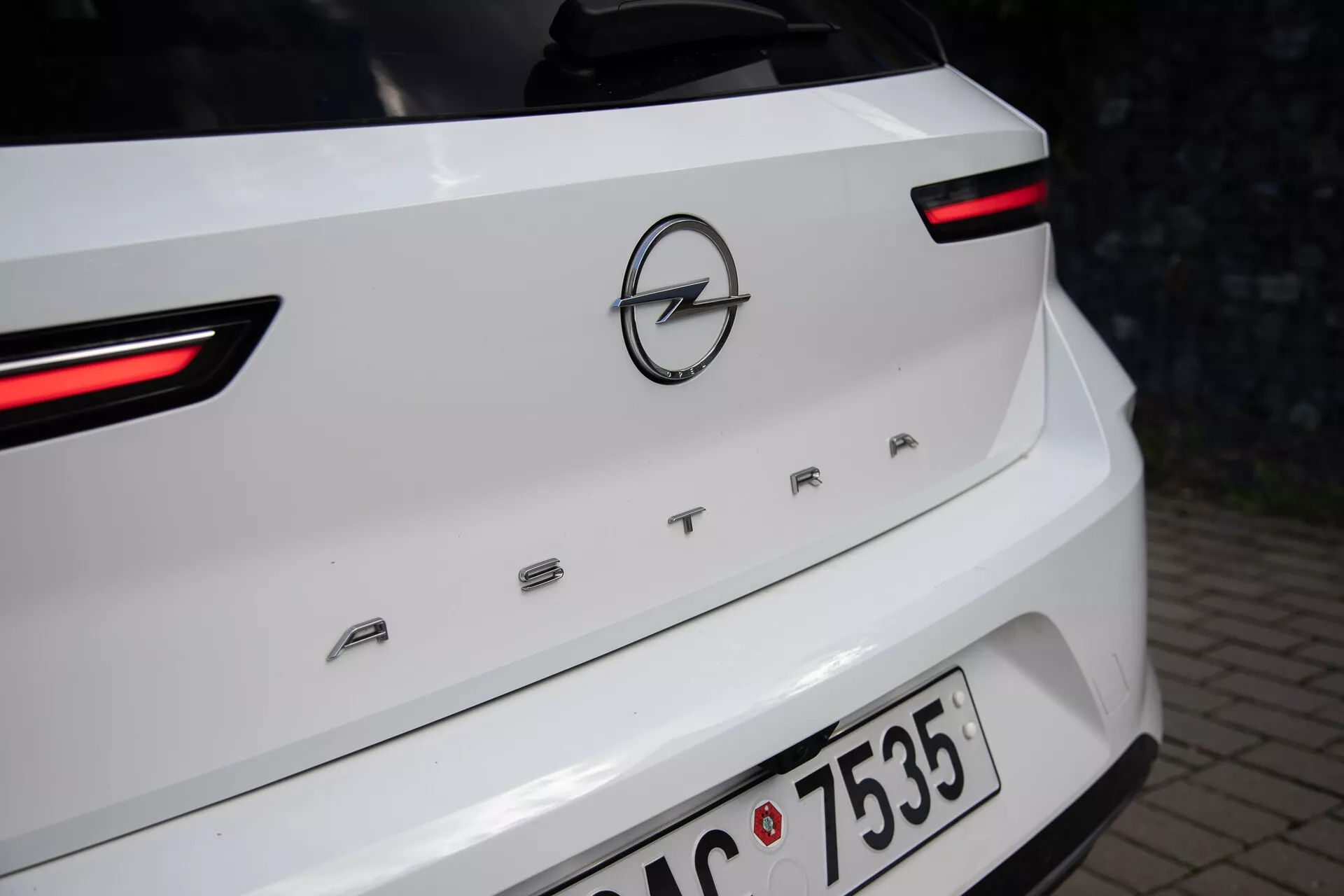 Zbliżony widok na tył białego Opel Astra z roku 2022, podkreślający LEDowe światła tylne, logo Opel i nazwę modelu 'ASTRA' na pokrywie bagażnika