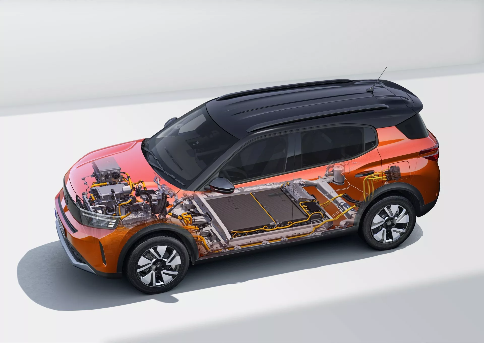 Widok z wysokiego kąta na model Opel Frontera 2024 (trzecia generacja) przedstawiający nowoczesny crossover lub kompaktowe SUV z pomarańczowym nadwoziem i czarnym dachem. Obrazek odsłania wewnętrzne komponenty, podkreślając wysokowoltowy akumulator biegnący wzdłuż podłogi, silnik(i) elektryczny(e) oraz elektronikę zasilającą. Widoczne są również aerodynamiczne felgi ze stopów metali lekkich. Pojazd ukazany jest w czystym, studyjnym otoczeniu, podkreślającym jego design i konstrukcję.