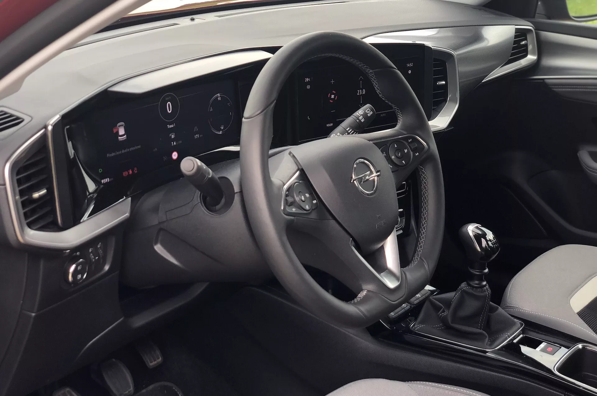 Widok wnętrza Opel Mokka 2021 z perspektywy pasażera siedzącego z tyłu po prawej stronie, prezentujący nowoczesną deskę rozdzielczą, wielofunkcyjną kierownicę, podświetlany cyfrowy zestaw wskaźników, system multimedialny z ekranem dotykowym, manualną dźwignię zmiany biegów oraz elegancki dwukolorowy design.