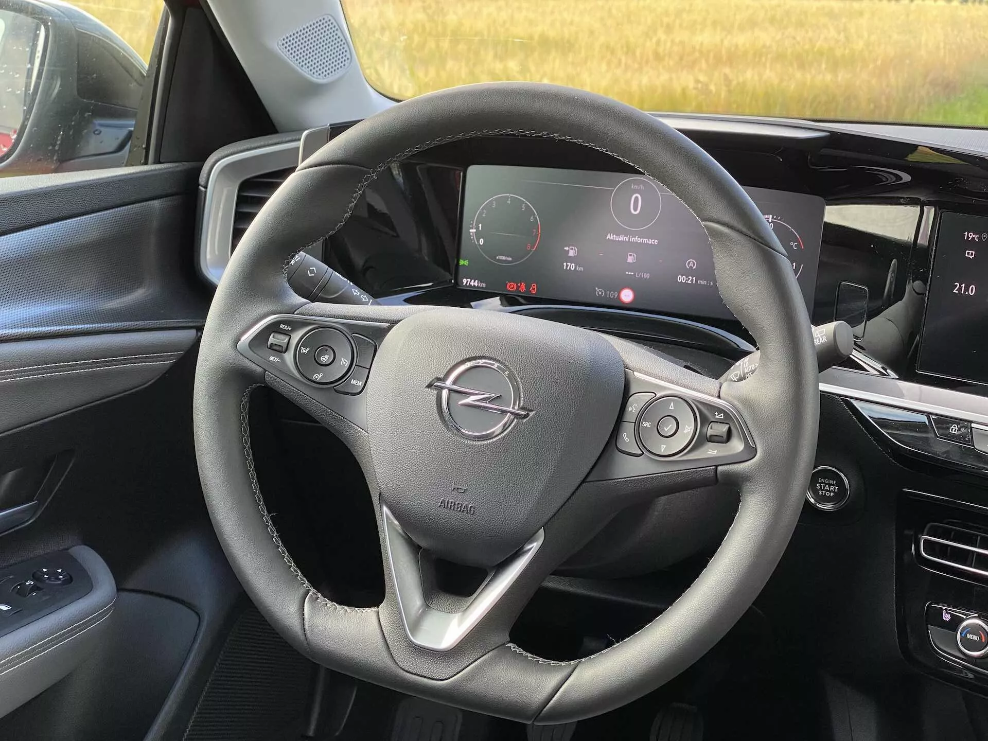 Widok wnętrza Opel Mokka 2021 z perspektywy fotela pasażera przedniego, prezentujący kierownicę z przyciskami do sterowania dźwiękiem i tempomatem, cyfrową deskę rozdzielczą wyświetlającą prędkościomierz i inne parametry, oraz konsolę środkową z dotykowym systemem infotainment.