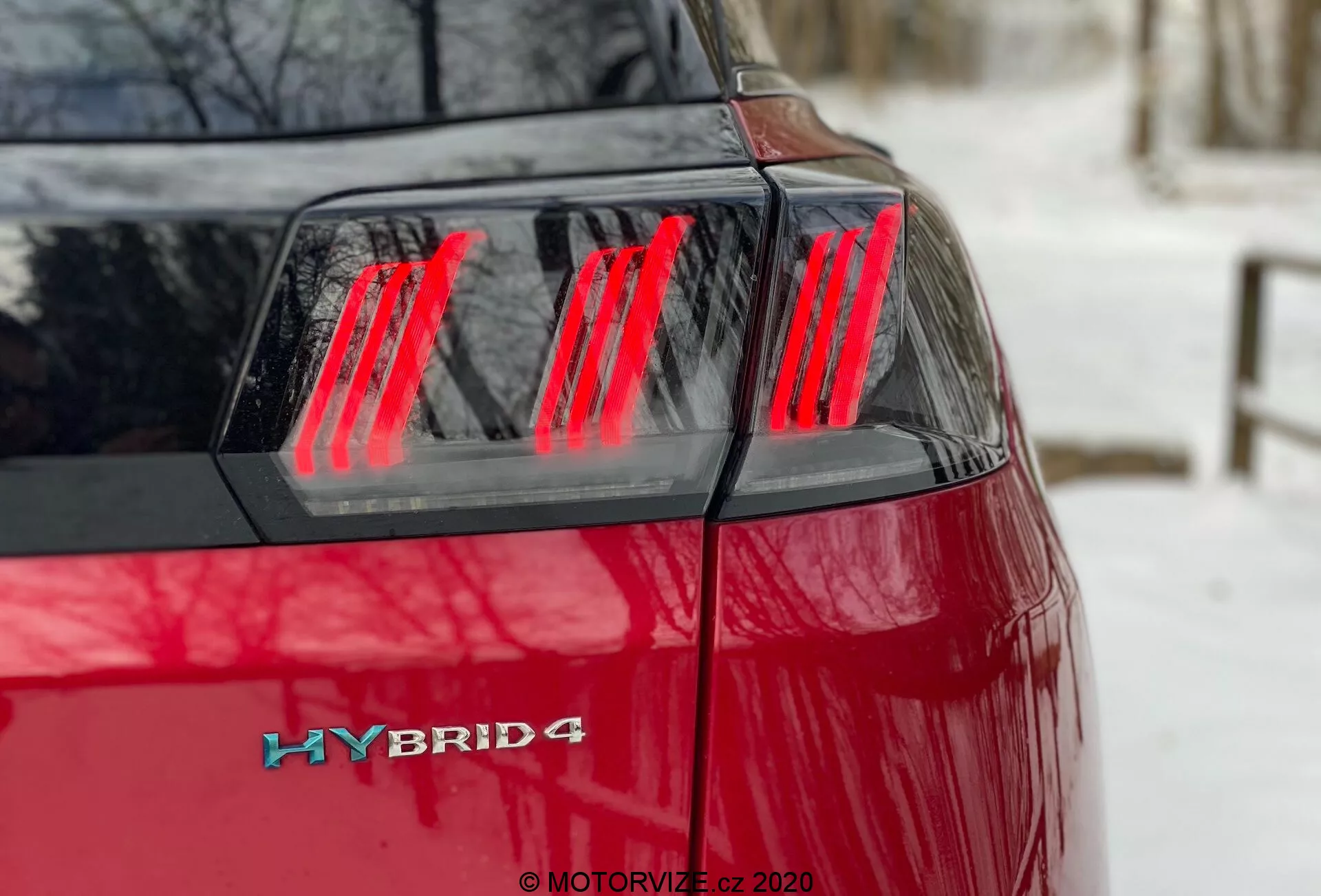 Peugeot 3008 Hybrid4 2021 - Zbliżenie lewego tylnego ćwiartki pod kątem, ukazujące żywy czerwony lakier, nowoczesny czerwony zespół świateł tylnych LED z wyraźnymi pionowymi segmentami, pokrywę bagażnika i odznakę hybrydową w lewym tylnym rogu, wskazującą na system napędu hybrydowego z możliwymi napęd na cztery koła.