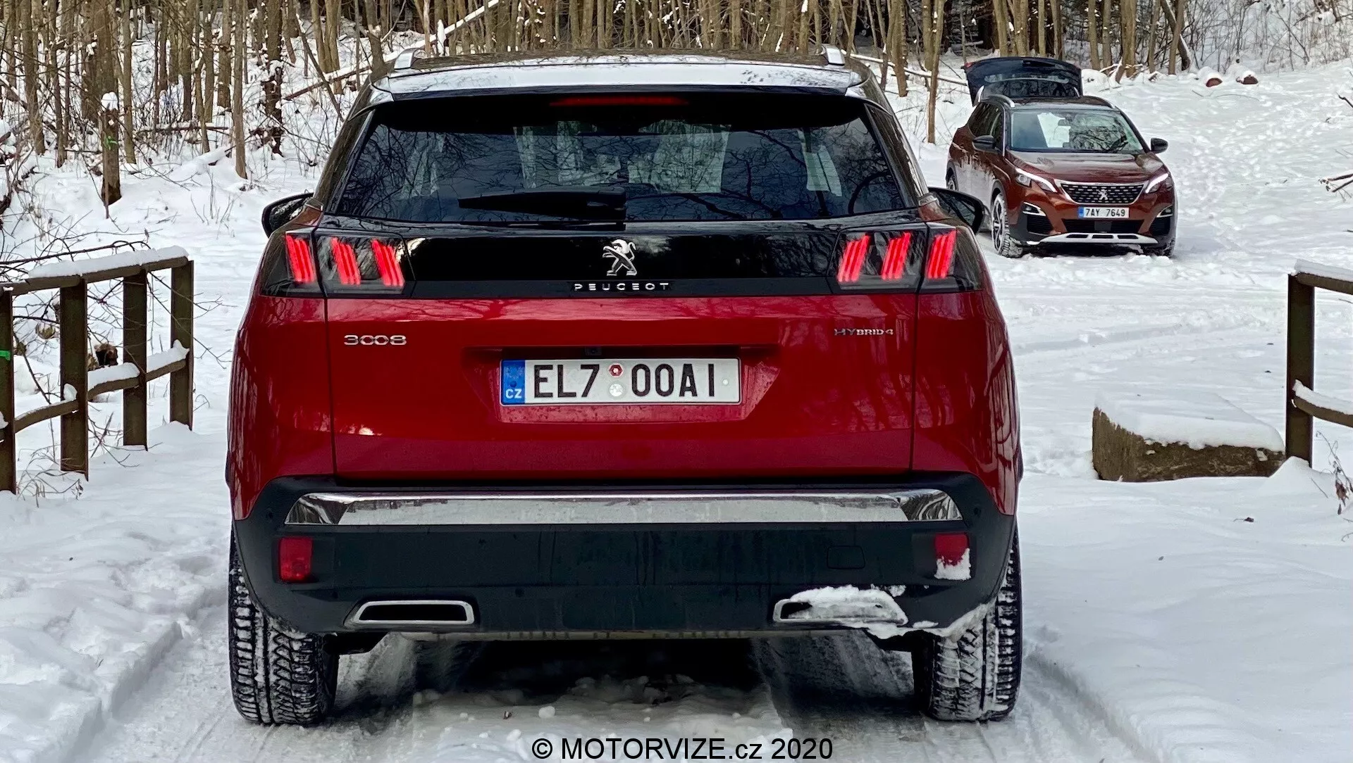 Widok z tyłu czerwonego SUV-a Peugeot 3008 uchwycony pod lekkim niskim kątem, który podkreśla charakterystyczne tylne światła w formie trzech pasków, centralne godło lwa Peugeot i dwukolorowy zderzak. Pojazd, umieszczony na pokrytej śniegiem ziemi, sugeruje zimowe warunki. Widoczne cechy obejmują tylne czujniki parkowania, tylną wycieraczkę i antenę na tylnej górnej części, co sugeruje technologię wspomagania kierowcy i potencjalną funkcjonalność GPS/radio, odpowiednie do dyskusji na temat projektowania samochodów, funkcji bezpieczeństwa i jazdy zimowej.