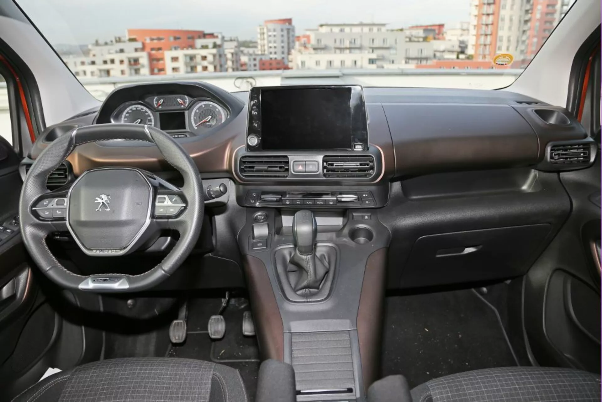 Widok wnętrza Peugeota 3008 z 2016 roku przedstawiający deske rozdzielczą, kierownicę z zamontowanymi sterowaniami i centralny dotykowy ekran systemu rozrywki z perspektywy tylnej kanapy