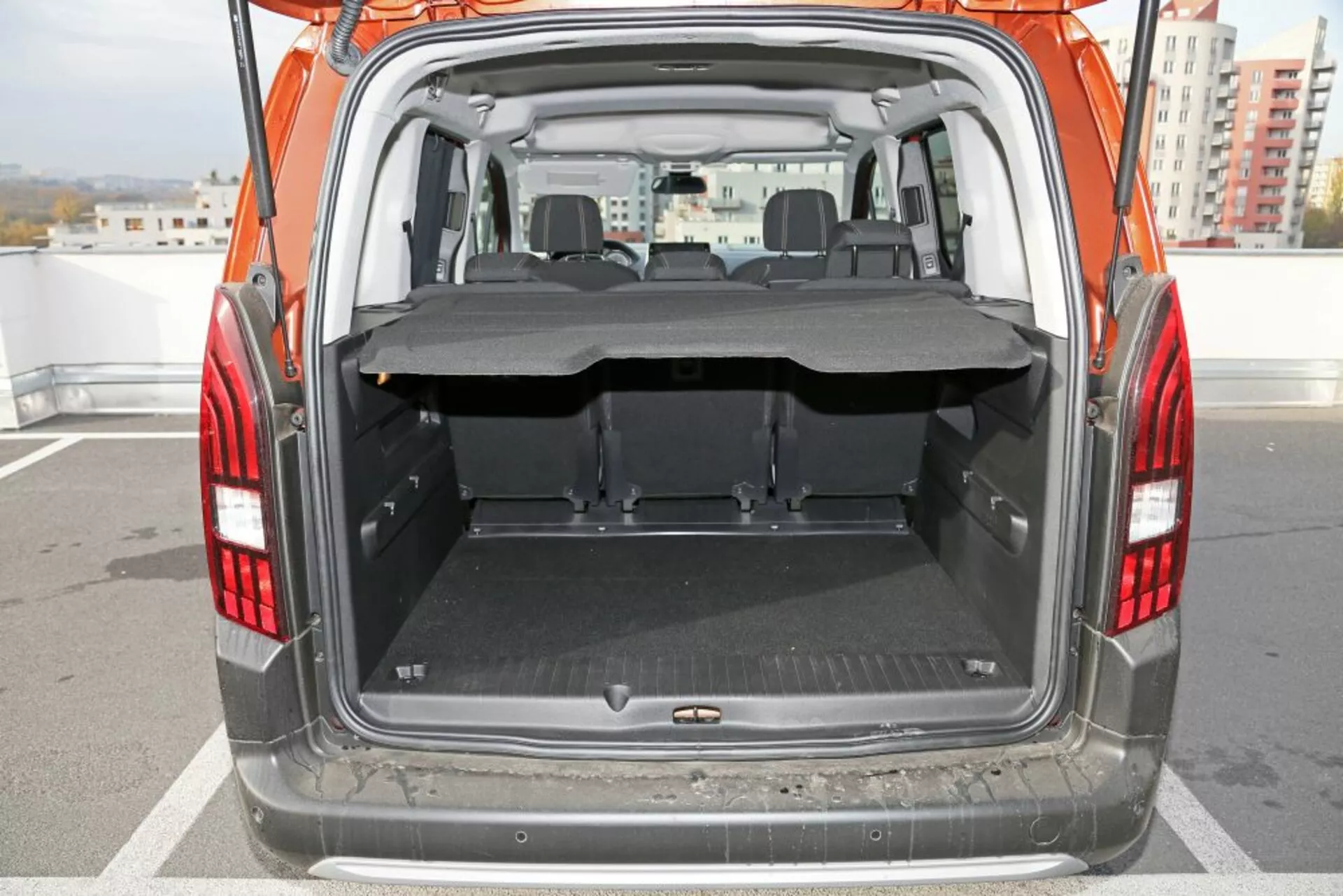Tylny widok SUV Peugeot 3008 z 2016 roku z naciskiem na otwarty bagażnik i przestrzeń ładunkową, prezentujący czystą płaską podłogę z ochronną matą, częściowo wysuniętą osłonę ładunku, składane tylne siedzenia i wyraźną widoczność przedniego obszaru siedzeń przez tył.