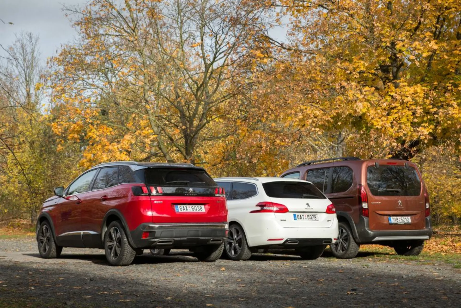 Tylny trzy czwarte widok Peugeota 3008 2016 w zewnętrznym, jesiennym otoczeniu, prezentujący czerwone SUV, białe kombi i brązowy kompaktowy MPV zaparkowane równolegle z naciskiem na cechy projektowe takie jak tylne światła, zderzak tylne i sylwetka.