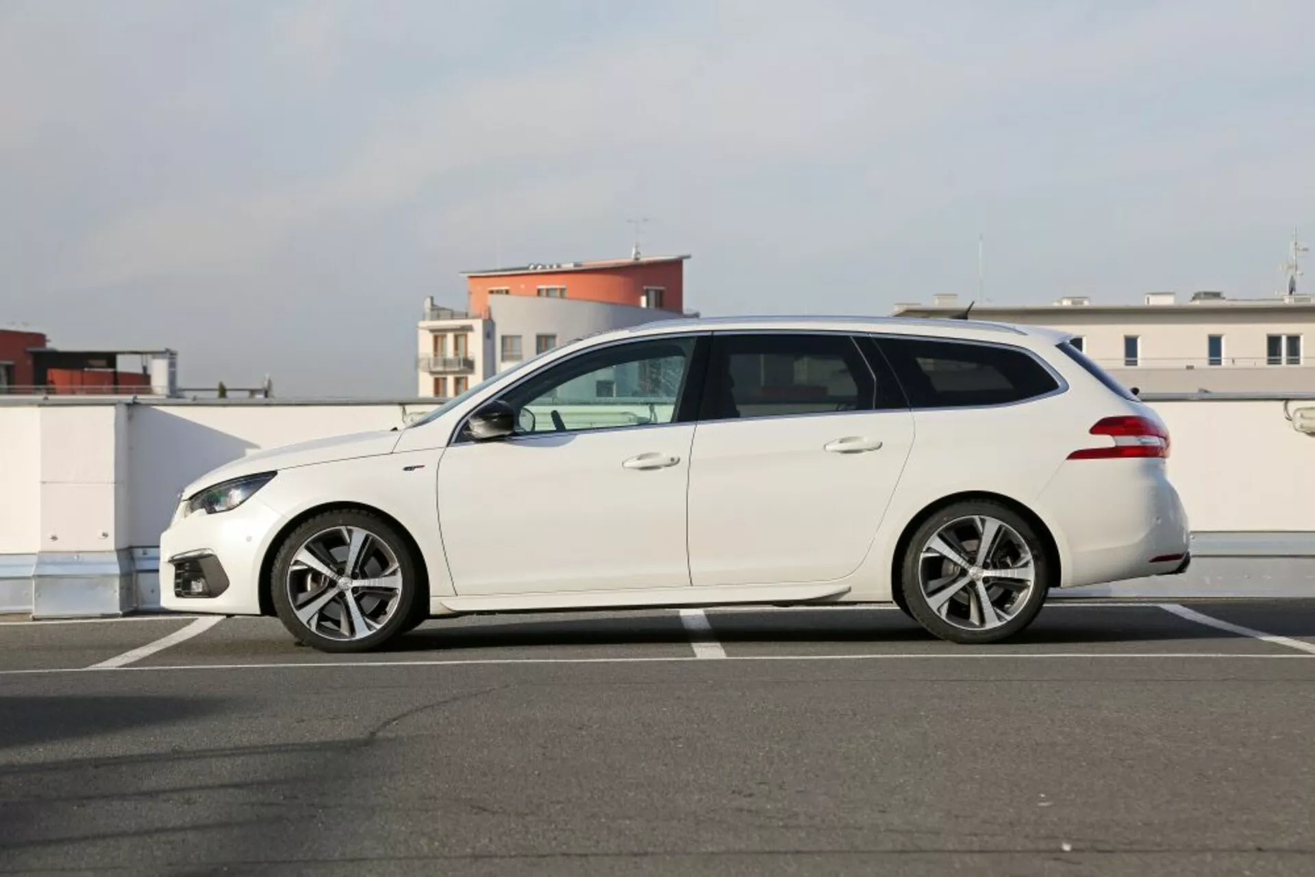 Biały kombi Peugeot 3008 z 2016 roku zaparkowany na asfalcie, widok z boku profilu prezentujący eleganckie reflektory, felgi aluminiowe wieloramienne, lusterka boczne w kolorze nadwozia i pięć drzwi