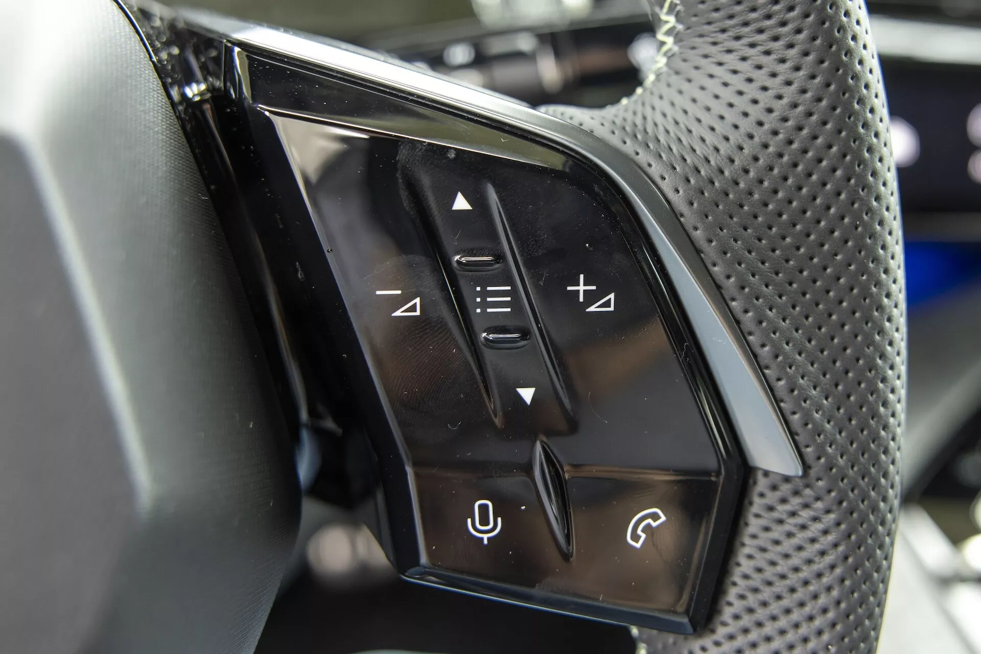 Zbliżenie panelu kontrolnego po stronie kierowcy na wewnętrznej stronie drzwi Peugeot 3008 2024 (e-3008), pokazujące przyciski do regulacji i składania lusterek bocznych, obrotowy regulator do wyboru lusterek, przycisk do automatycznego opuszczania i podnoszenia szyb elektrycznych oraz przycisk blokady szyb na panelu o teksturze z włókna węglowego, koncentrując się na cechach projektowych samochodu i atrybutach luksusowych.