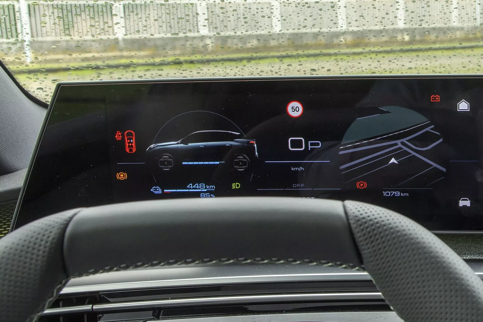 Zbliżenie wnętrza Peugeot 3008 2024 (e-3008), podkreślające cyfrowy panel instrumentów i system informacyjno-rozrywkowy zintegrowany w jednym szerokim, poziomym wyświetlaczu. Z perspektywy kierowcy, podświetlany ekran pokazuje stacjonarny prędkościomierz na 0 km/h, pełny wskaźnik paliwa i wskaźniki świateł awaryjnych po lewej stronie; zaawansowane systemy wspomagania kierowcy i stan parkowania po prawej stronie; oraz całkowity przebieg, przebieg podróży i status baterii na dole. Wyświetlacz podkreśla nowoczesne trendy w technologii motoryzacyjnej w kierunku digitalizacji i systemów informacyjnych dla kierowców, w luksusowym, high-techowym środowisku.