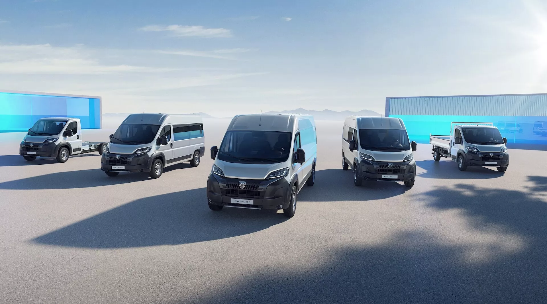 Obraz przedstawiający linię pięciu vanów Peugeot 3008 2024 w różnych modelach, ustawionych w formacji stopniowej. Van najbliżej kamery jest uchwycony pod kątem trzech czwartych z przodu, podkreślając jego nowoczesny design z eleganckimi liniami, reflektorami LED, przednim grillem, światłami przeciwmgielnymi i przednią szybą. Pojazdy za nim są ustawione diagonalnie, tworząc wrażenie głębi, a każdy z nich jest uchwycony pod podobnym kątem trzech czwartych z przodu, ukazując ich wielofunkcyjność z elementami takimi jak boczne lusterka i boczne panele. Sceneria wydaje się być w otwartym kompleksie przemysłowym lub komercyjnym ze słonecznym niebem i jasnym, naturalnym światłem.