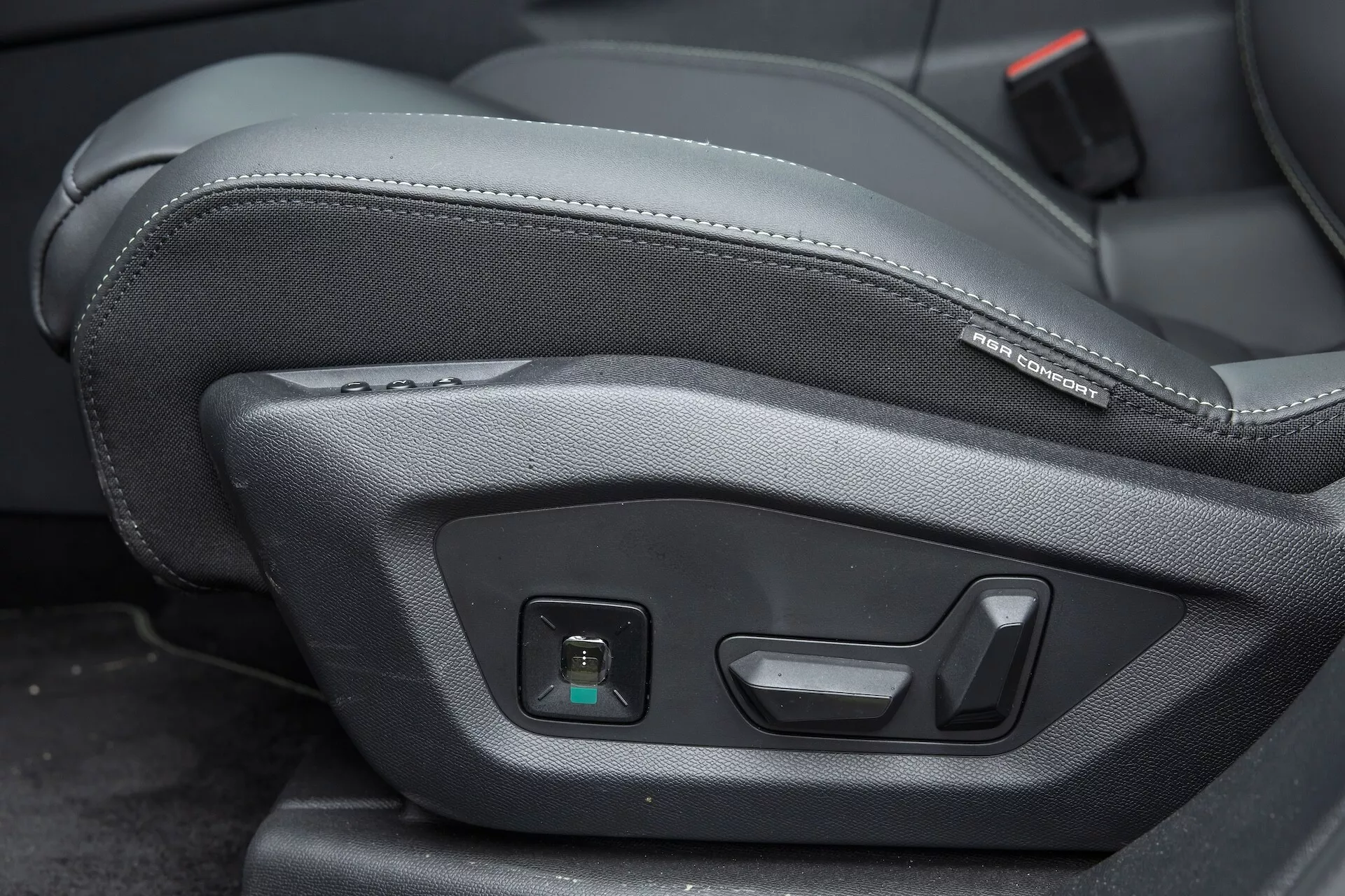 Zbliżenie na sterowanie elektrycznym ustawieniem fotela w Peugeot 3008 2024 (e-3008), podkreślające technologiczne funkcje regulacji ustawienia siedzenia, w tym przesuwanie fotela do przodu lub do tyłu, regulację kąta nachylenia oparcia oraz podparcia lędźwiowego. Przyciski znajdują się z boku fotela kierowcy lub pasażera, mają nowoczesny i ergonomiczny design oraz matowe wykończenie na ciemnej tapicerce przypominającej skórę. Zdjęcie wykonane z wysokiego kąta podkreśla komfort i funkcjonalność wnętrza samochodu.