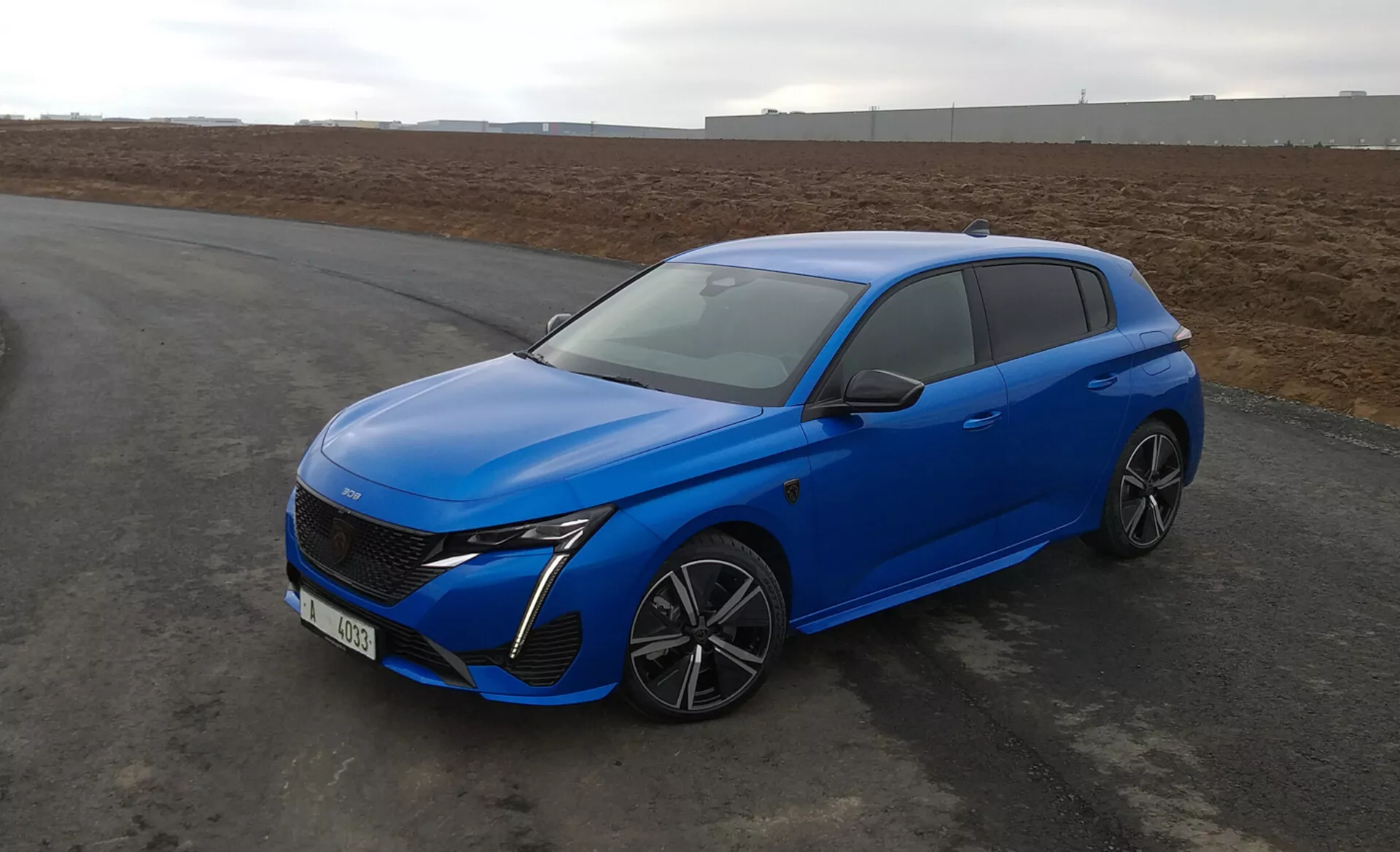 Peugeot 308 hatchback 2022 w jasnym niebieskim kolorze, z aerodynamicznym designem, reflektorami LED, zaawansowaną przednią grillą, felgami aluminiowymi o wielu szprychach i nowoczesnymi funkcjami bezpieczeństwa, zaparkowany na asfalcie