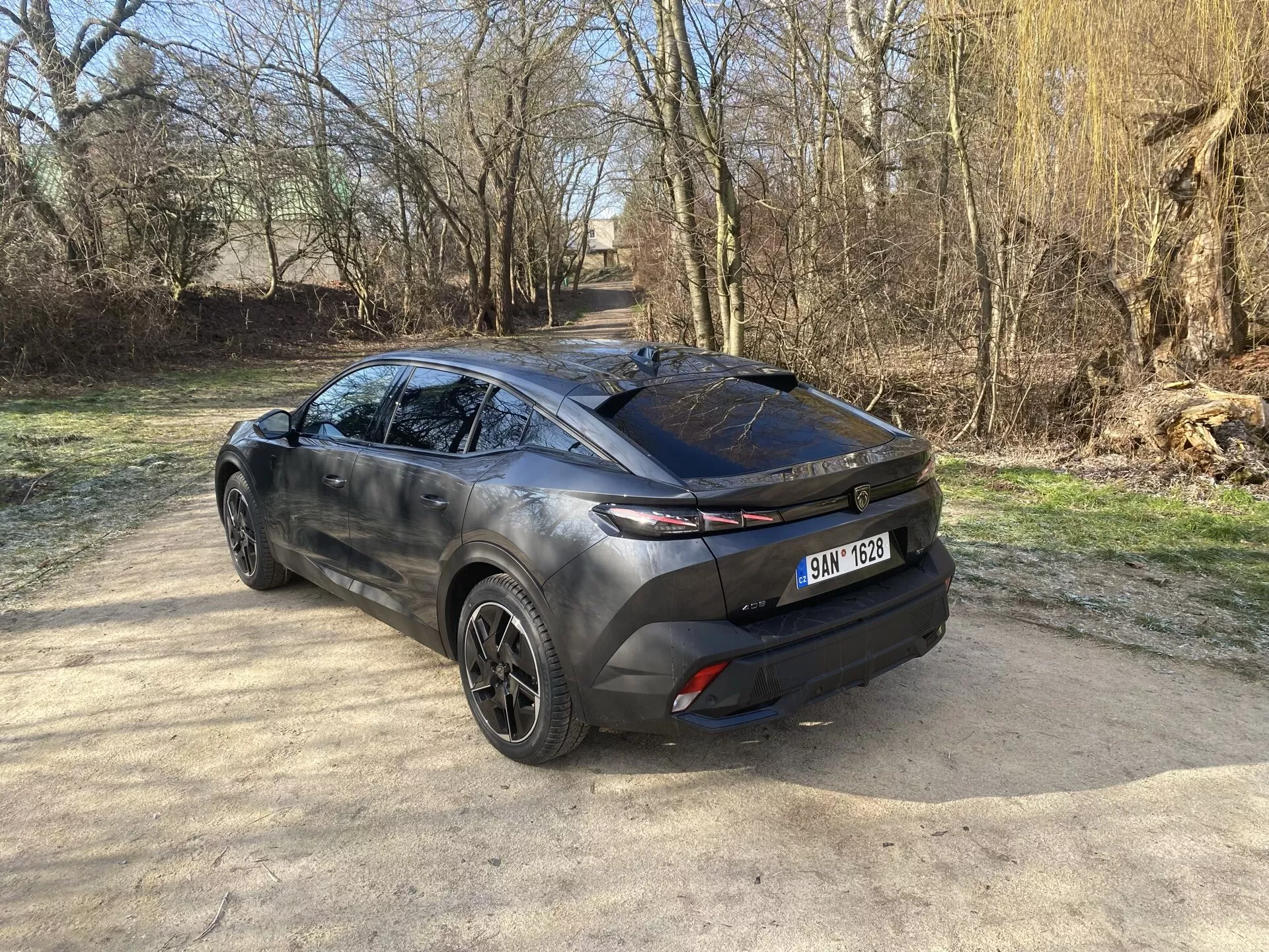 Tylny widok trzy czwarte Peugeota 408 2023 prezentujący jego nowoczesny design crossover, podkreślający klapę bagażnika, elegancką tylną szybę i poziome tylne światła rozciągające się na bok karoserii, z widokiem na felgi aluminiowe, rzeźbiony profil boczny i dwukolorową karoserię w naturalnym świetle słonecznym