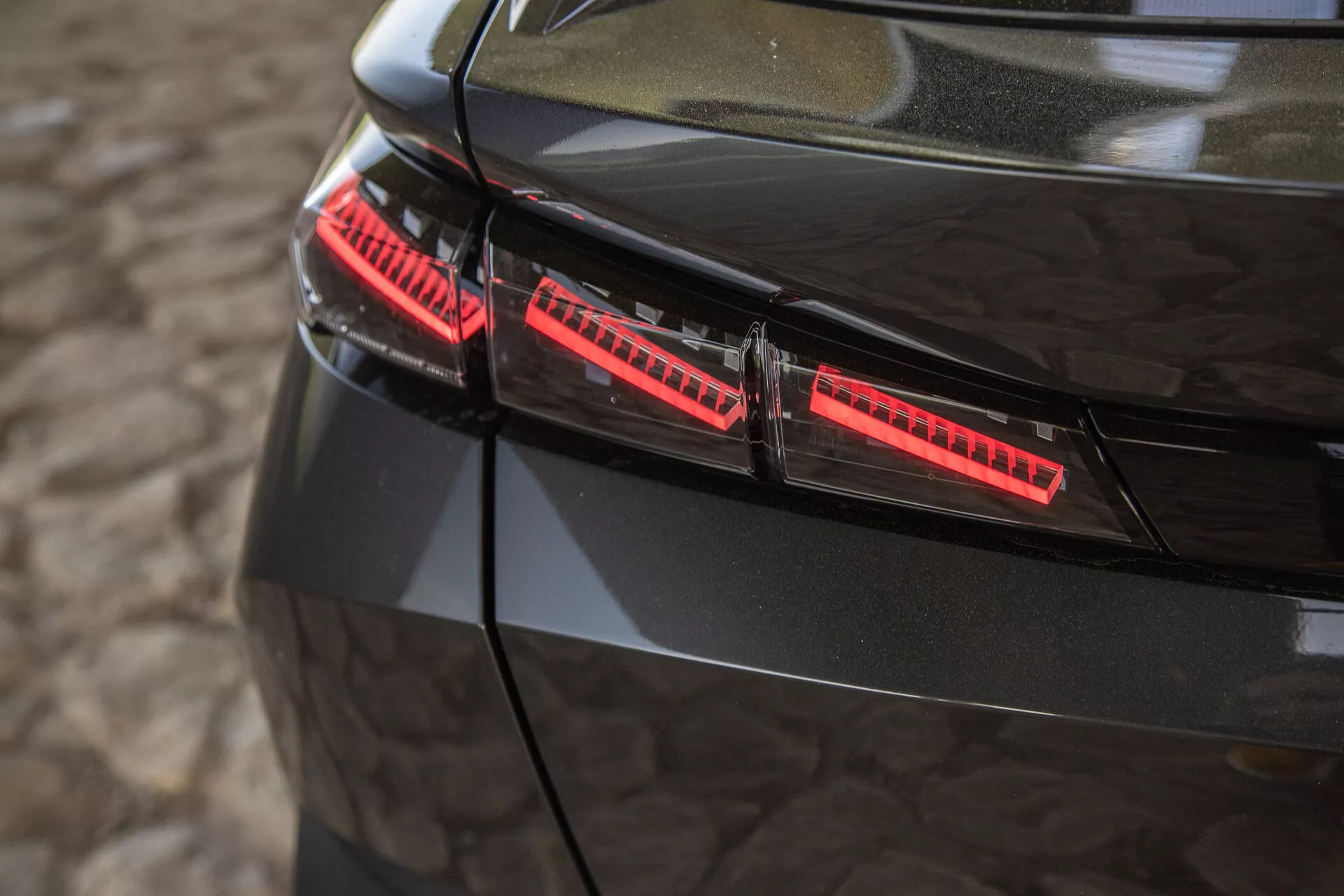 Zbliżenie na lśniące czarne tylne światła Peugeota 408 z 2023 roku, z nowoczesnymi elementami LED i eleganckimi akcentami designu, uchwycone z lekko podniesionego kąta