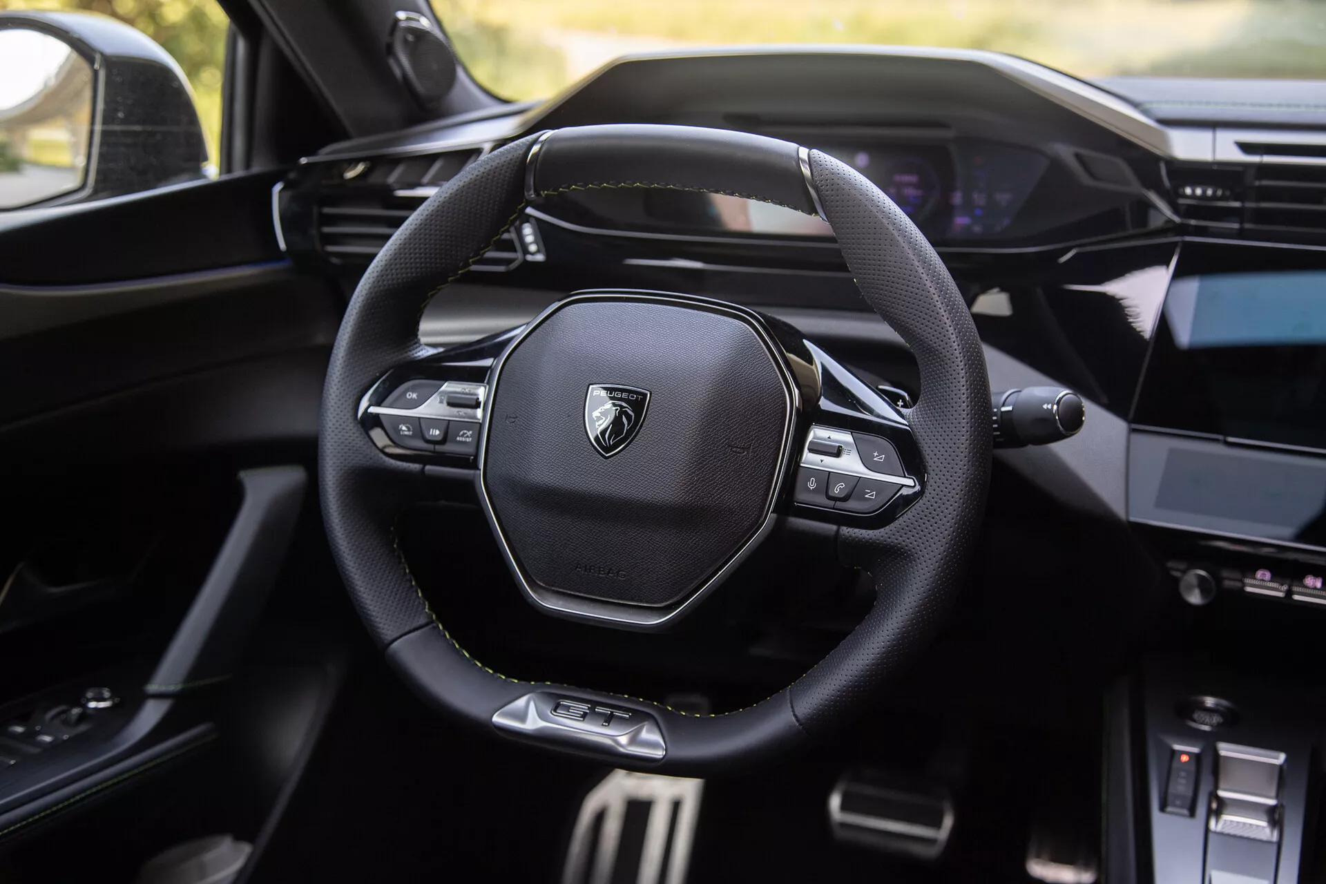 Wnętrze Peugeota 408 z 2023 roku z nowoczesną wielofunkcyjną kierownicą z logo marki, cyfrowym kokpitem w tle i częściowo widoczną konsolą środkową z systemem infotainment