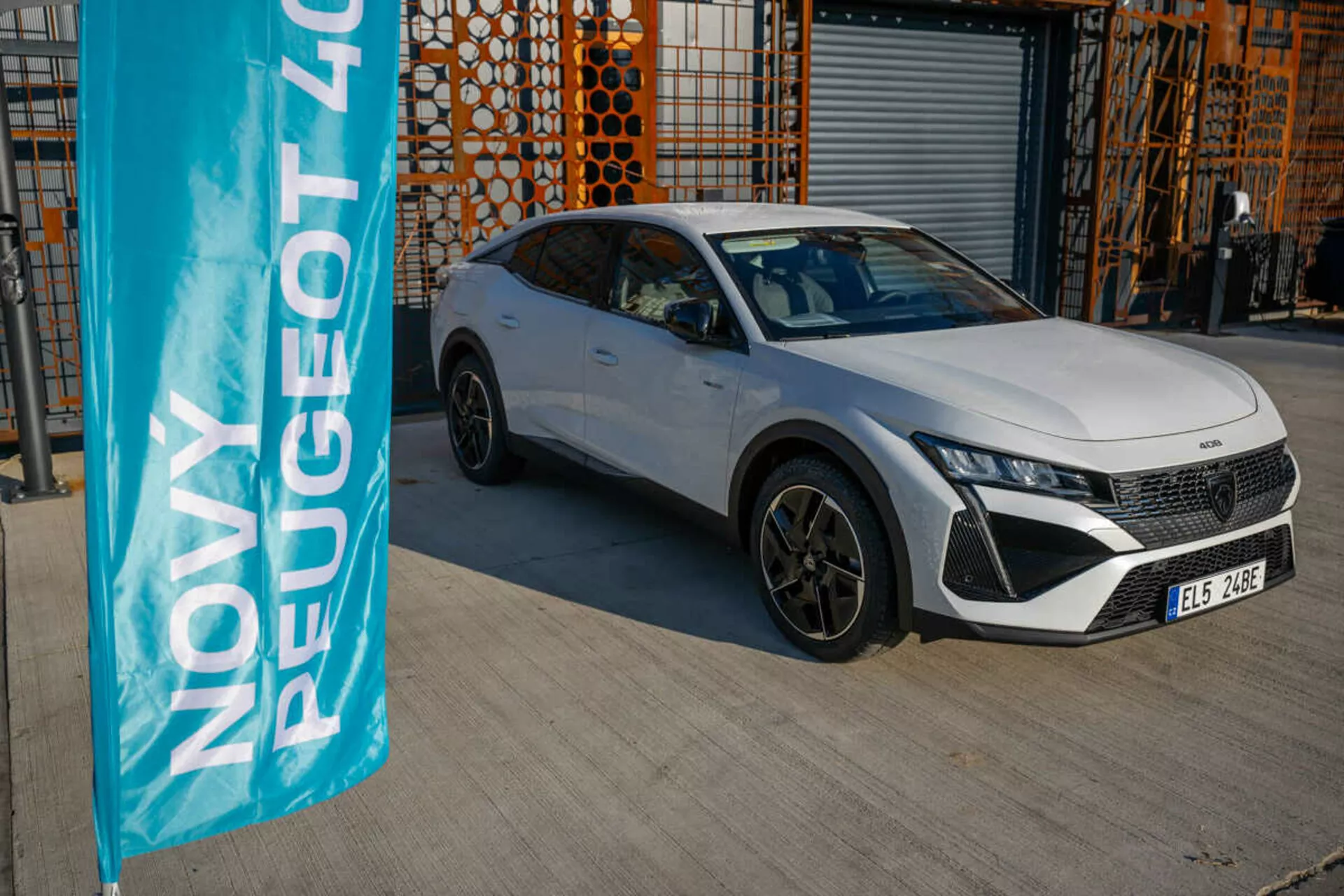Biały Peugeot 408 z 2023 roku zaparkowany na zewnątrz z architekturą przemysłową w tle, prezentujący funkcje projektowe i technologiczne pojazdu w naturalnym świetle dziennym