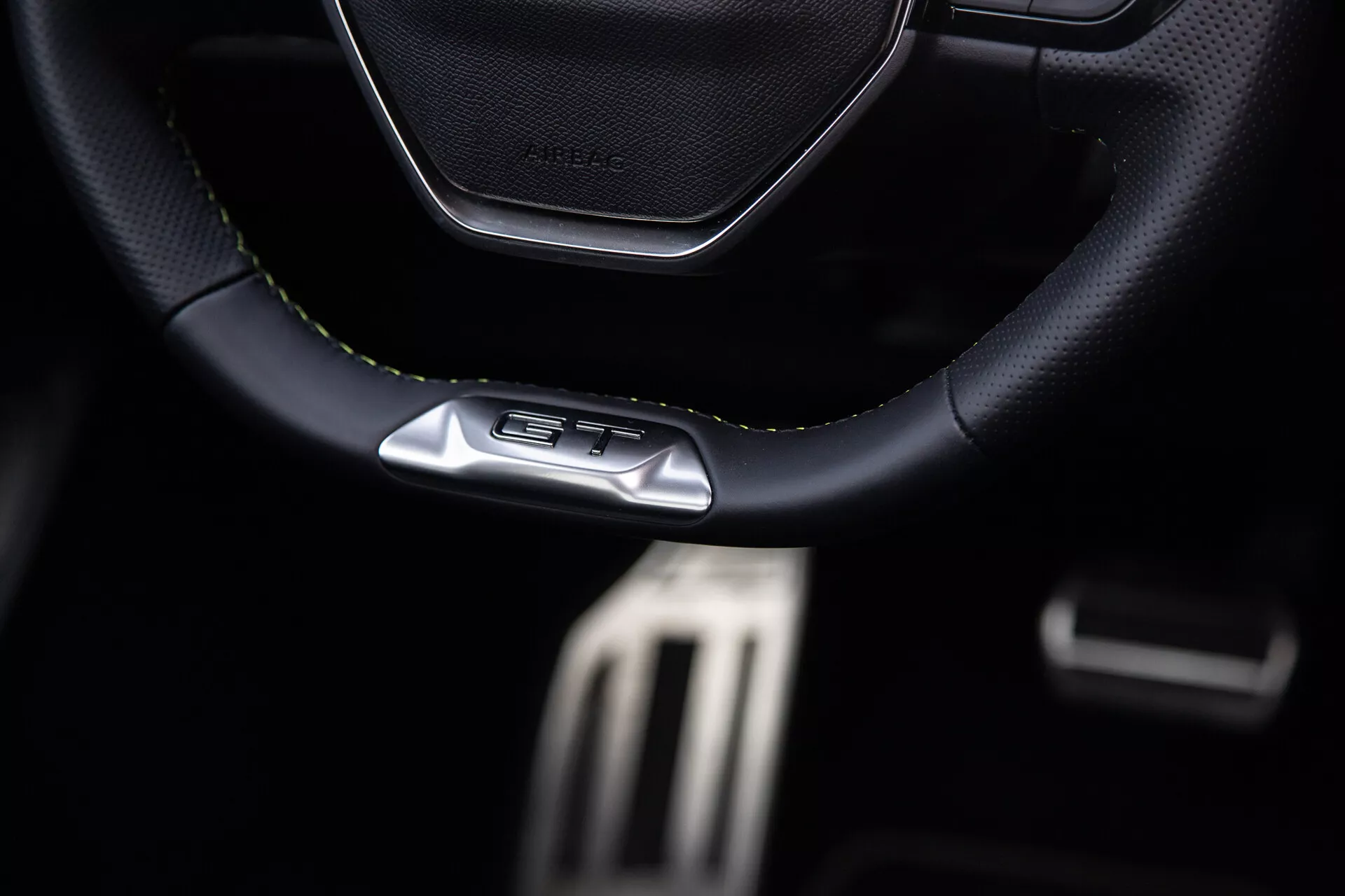 Wnętrze Peugeota 408 z 2023 r., skupiające się na sportowej kierownicy z przeszyciami skórzanych lub skóropodobnych z emblematem GT, metalowych pedałach o wysokiej wydajności i cechach premium ciemnej kabiny