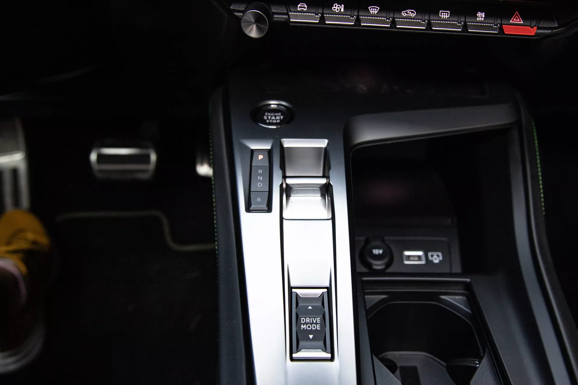 Zbliżenie na konsolę środkową Peugeot 408 2023 z dźwignią zmiany biegów w pozycji Park, przyciskiem TRYB JAZDY, elektronicznym hamulcem postojowym i portami USB, prezentujące nowoczesny design wnętrza.
