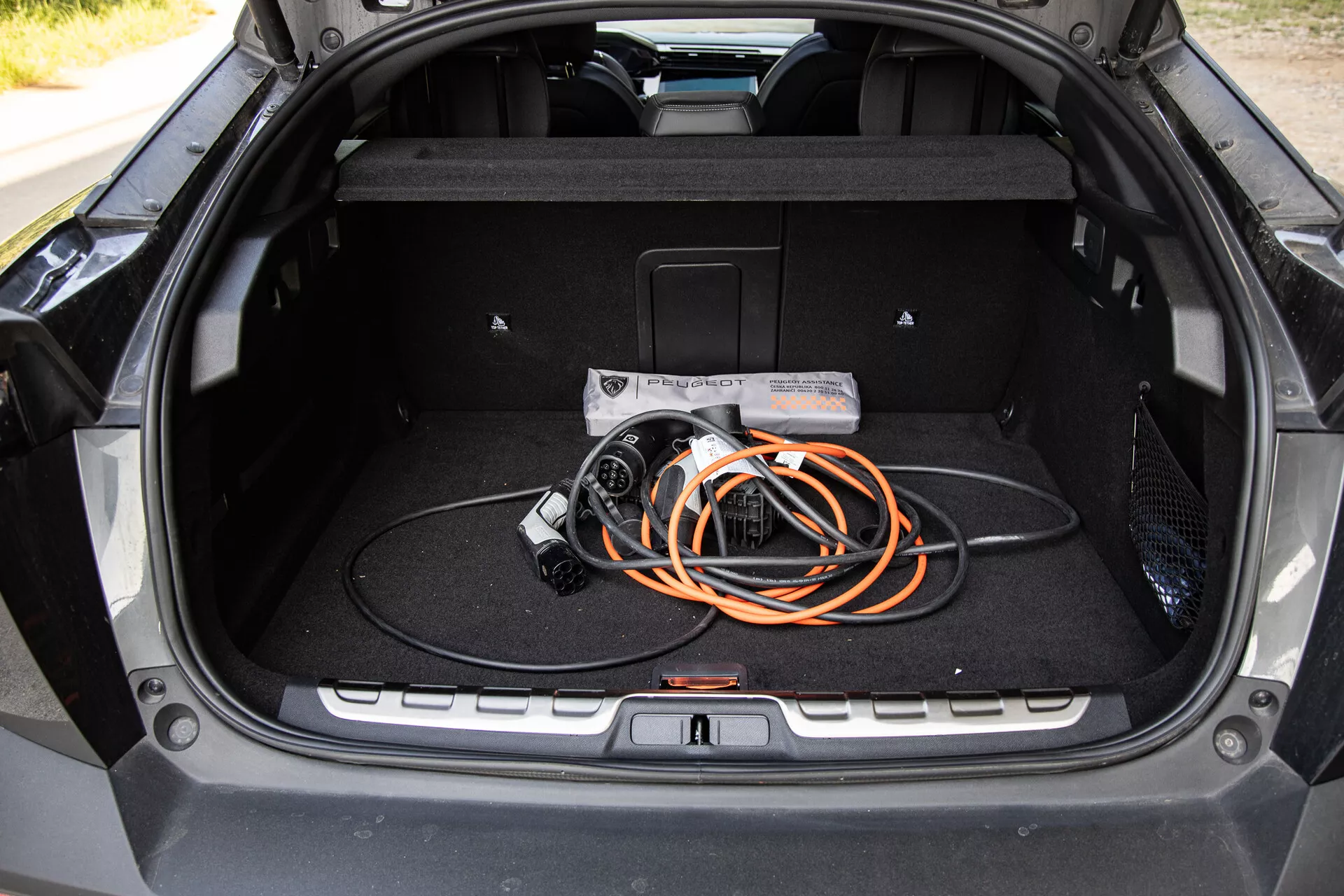 Widok wnętrza bagażnika Peugeot 408 2023, prezentujący przestronną konstrukcję i kabel do ładowania pojazdów elektrycznych, podkreślający technologię EV i nowoczesną jakość budowy.