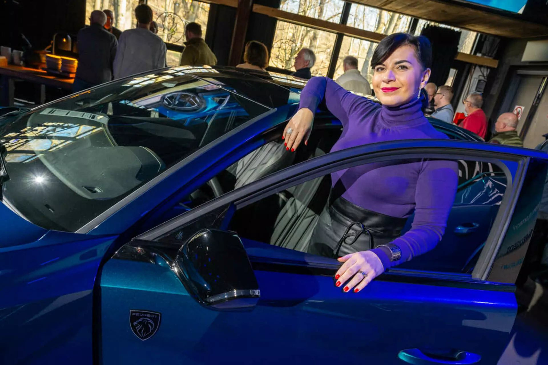 Wibrujący niebieski samochód sportowy, prawdopodobnie Lamborghini, uchwycony z kąta trzy czwarte podkreślający jego eleganckie linie, ostre światła LED i ikoniczne logo w kształcie tarczy, z osobą swobodnie oddziałującą z pojazdem sugerującą luksus i styl.